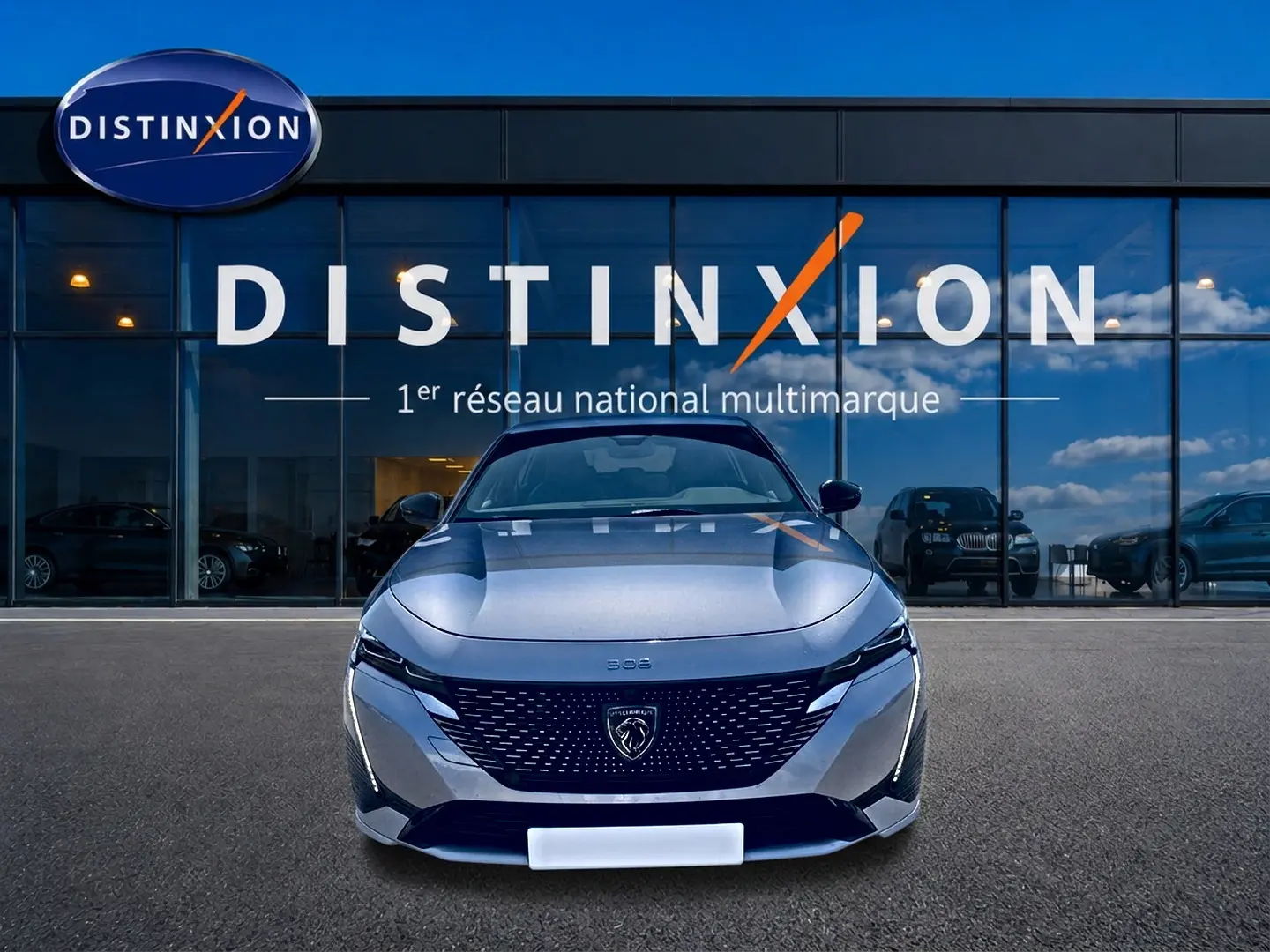 Vue frontale d'une Peugeot 308 gris métallisé 2025 avec calandre noire et logo lion distinctif, devant un showroom Distinxion.