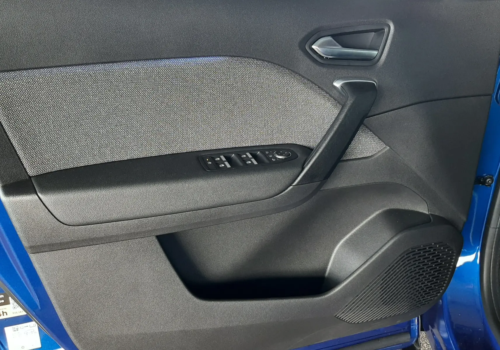 Vue intérieure de la porte avant gauche du Renault Captur bleu iron, avec commandes de vitres et tissu gris.