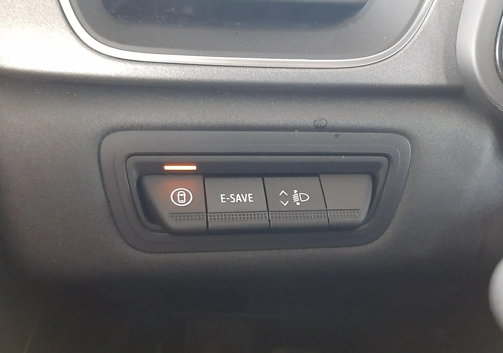 Gros plan sur les commandes E-SAVE et réglage des phares dans l'habitacle noir du Renault Captur E-Tech Hybrid 2024.