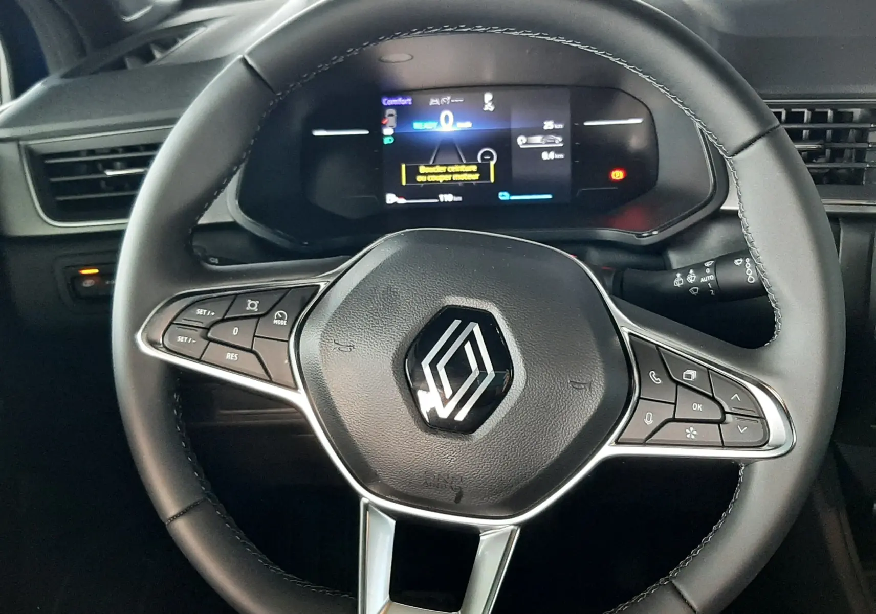 Volant noir avec logo Renault au centre, tableau de bord numérique affichant les informations de conduite, intérieur sombre.