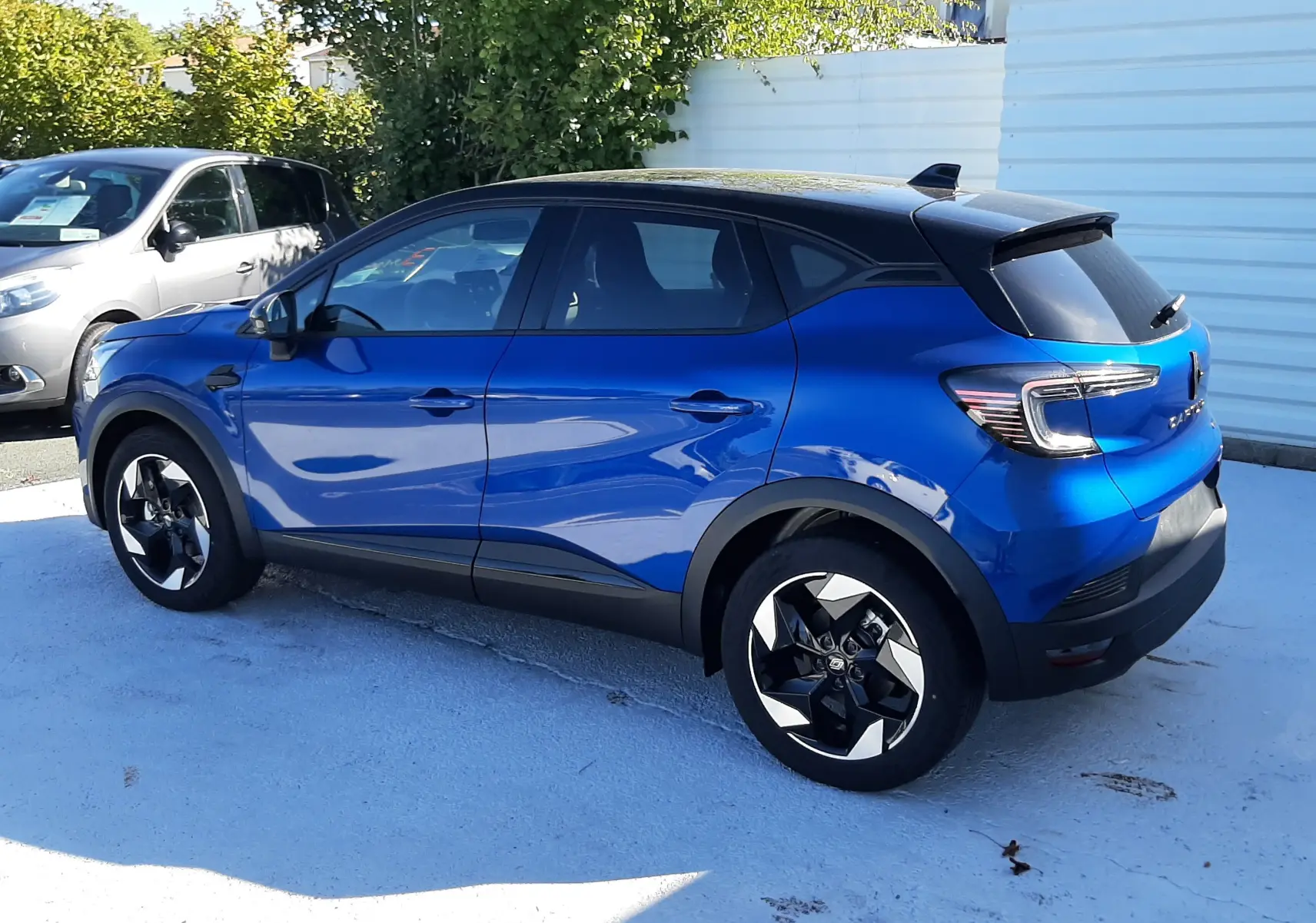 Renault Captur E-Tech Hybrid bleu Iron avec toit noir, vue côté gauche arrière en extérieur sous soleil.