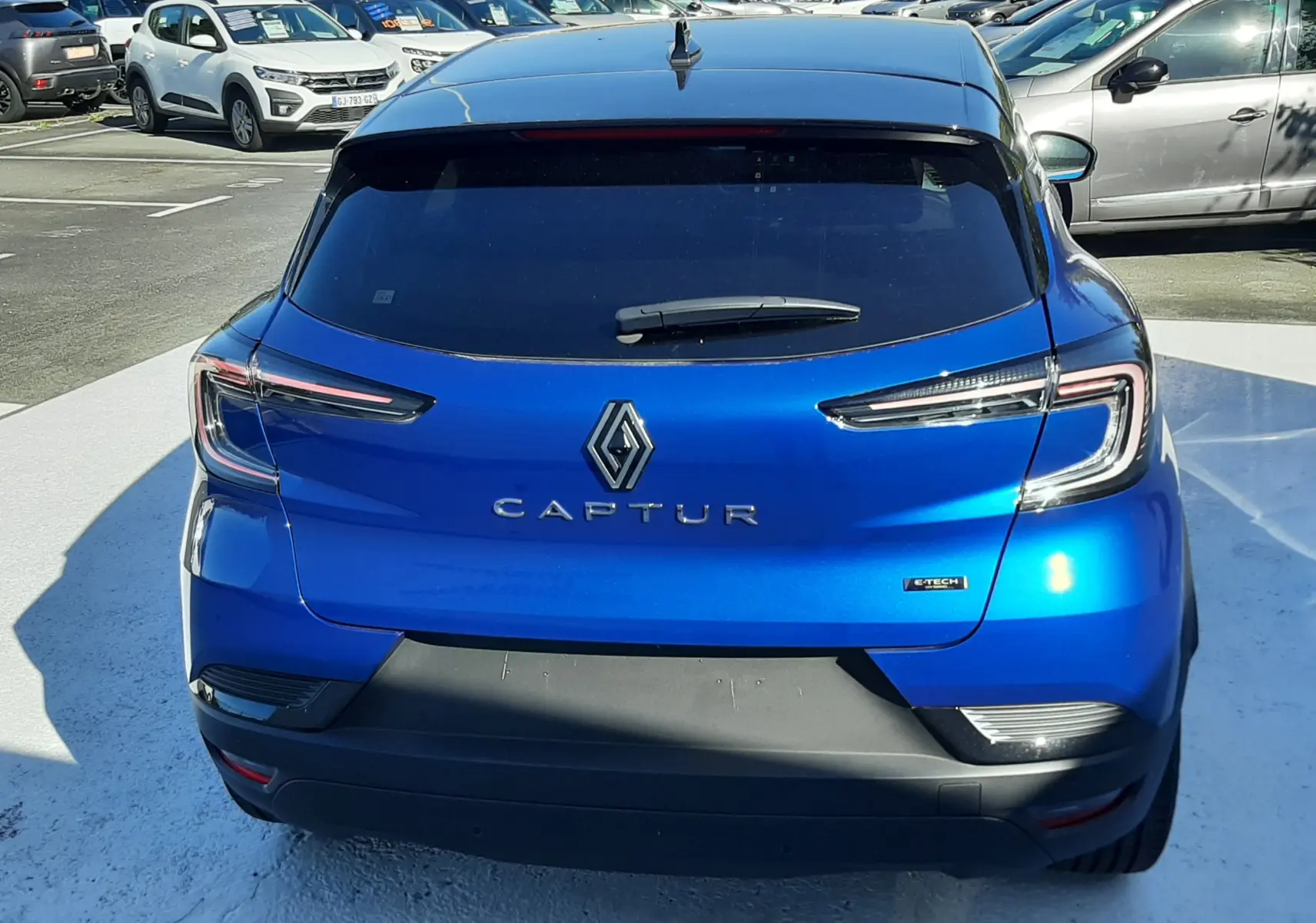 Vue arrière d'un Renault Captur E-Tech Hybrid 145ch bleu iron avec toit noir, feux LED et logo distinctif au centre.
