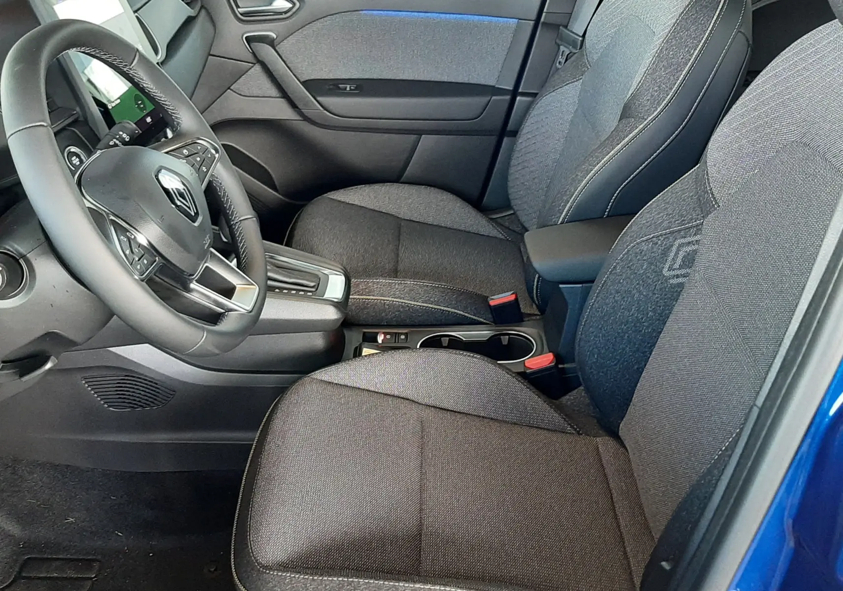 Intérieur avant droit du Renault Captur E-Tech Hybrid 2024, sièges gris foncé avec surpiqûres et détails bleus, volant multifonction.