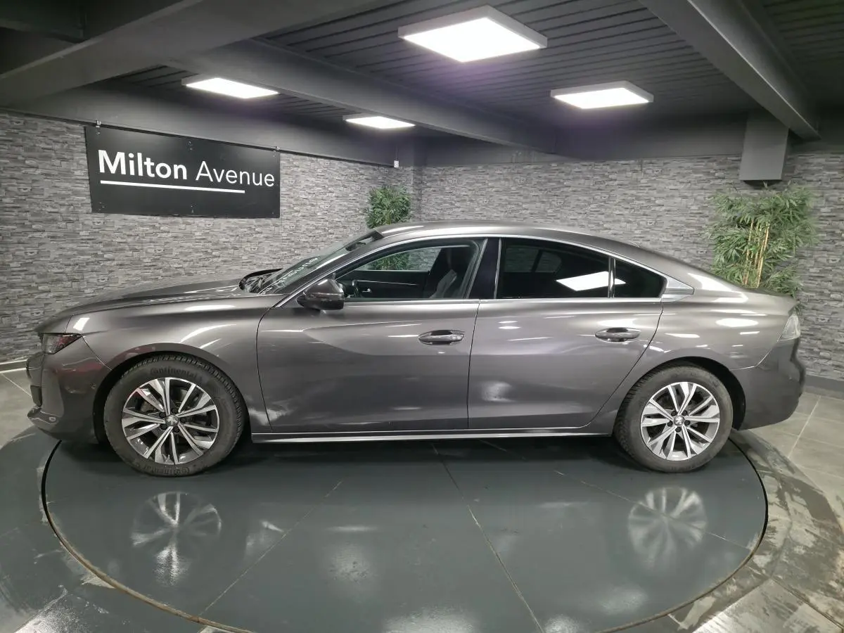Profil côté gauche d'une Peugeot 508 gris métallisé 2018 avec jantes alliage et vitres surteintées en intérieur showroom.