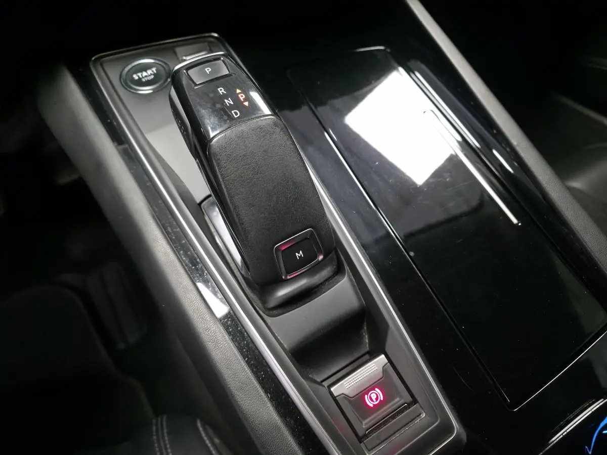 Gros plan sur la console centrale noire brillante de la Peugeot 508 gris, avec levier de vitesse automatique et frein à main électrique.