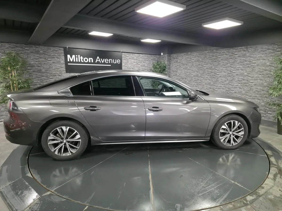 Profil côté gauche d'une Peugeot 508 gris métallisé, avec jantes alliage et lignes élégantes dans un showroom.