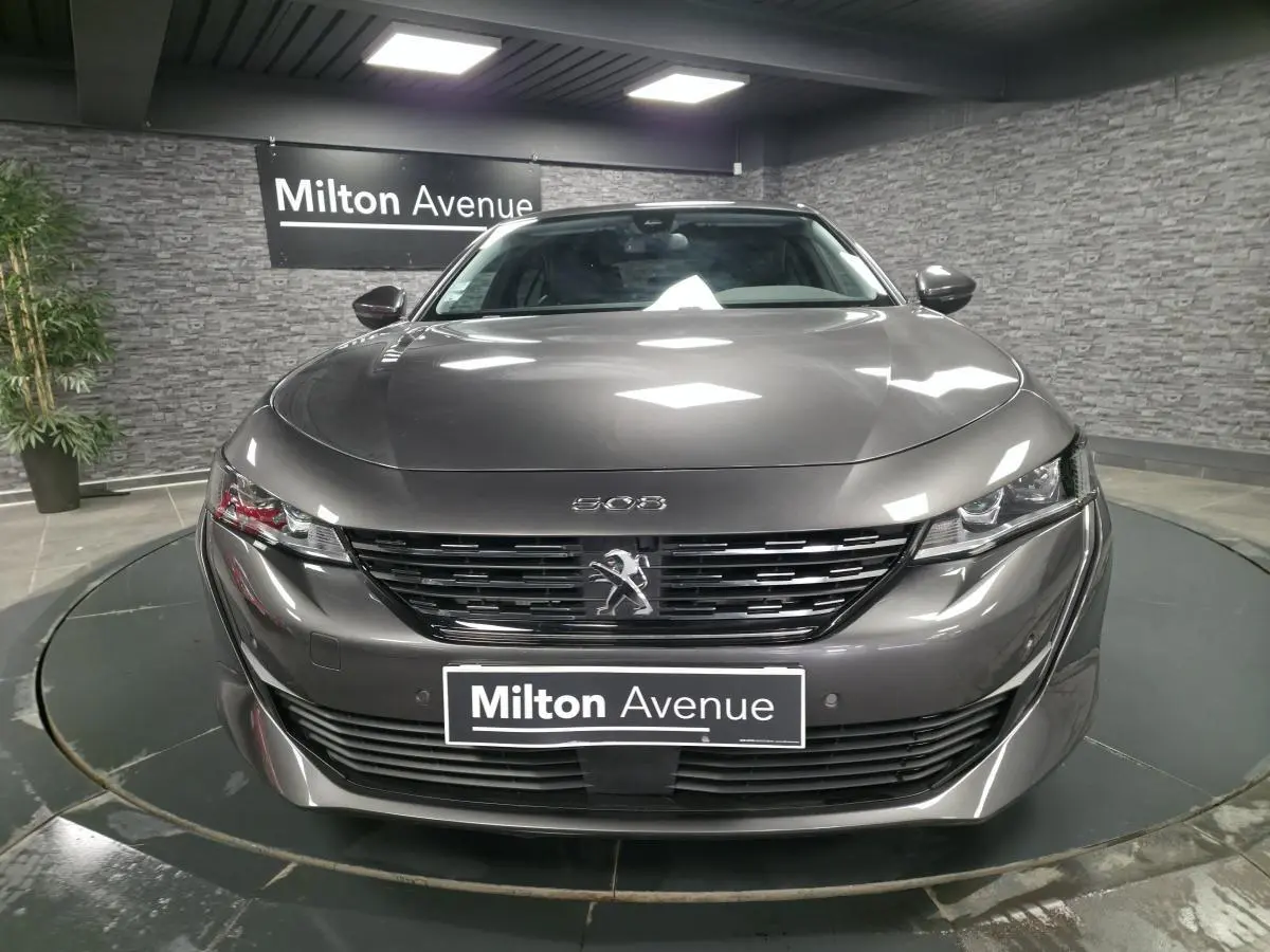 Peugeot 508 gris métallisé vue de face avec calandre noire et logo lion au centre, en showroom.