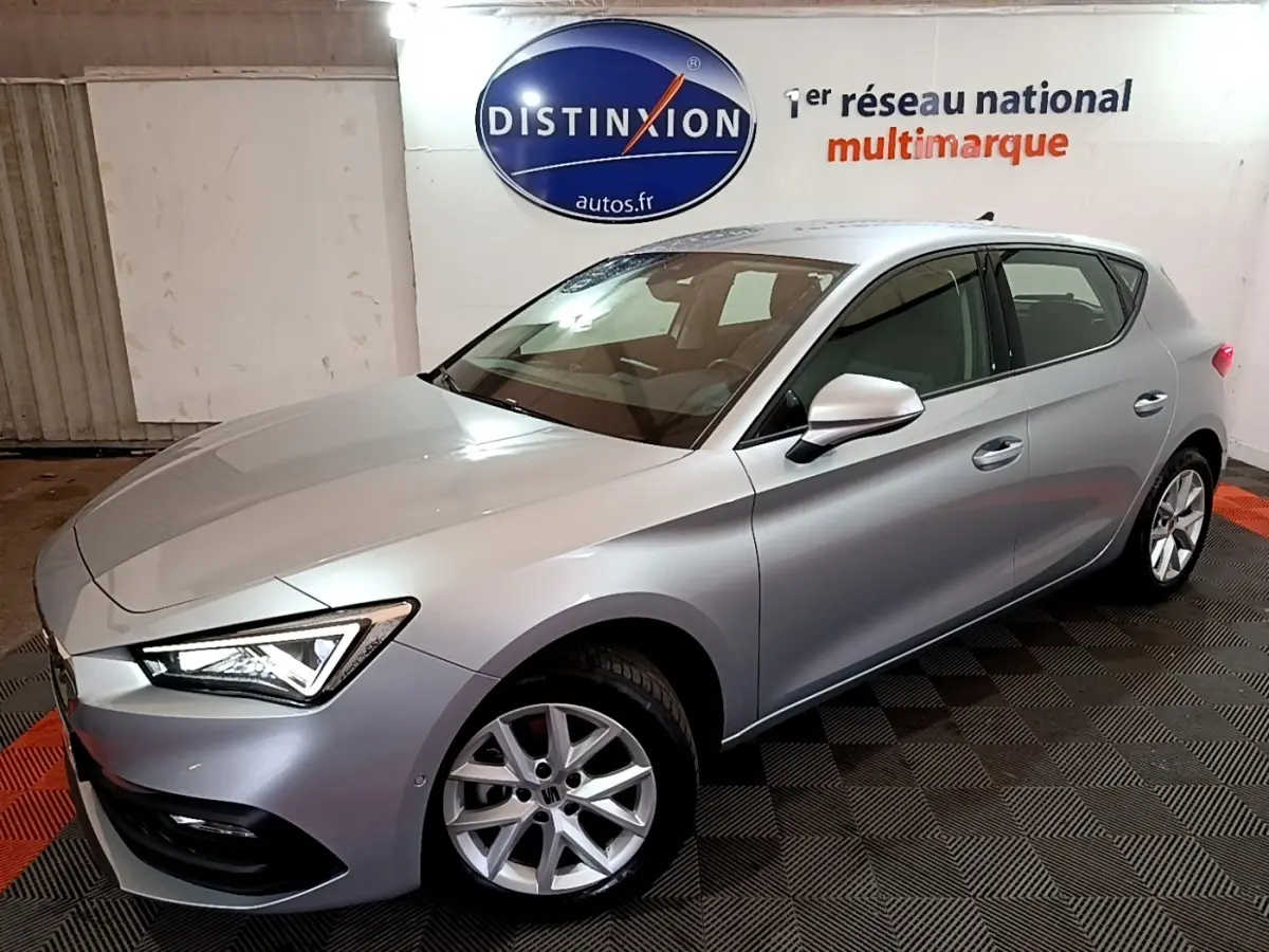 SEAT Leon gris foncé vue 3/4 avant droit dans un showroom avec éclairage intérieur et logo Distinxion en arrière-plan