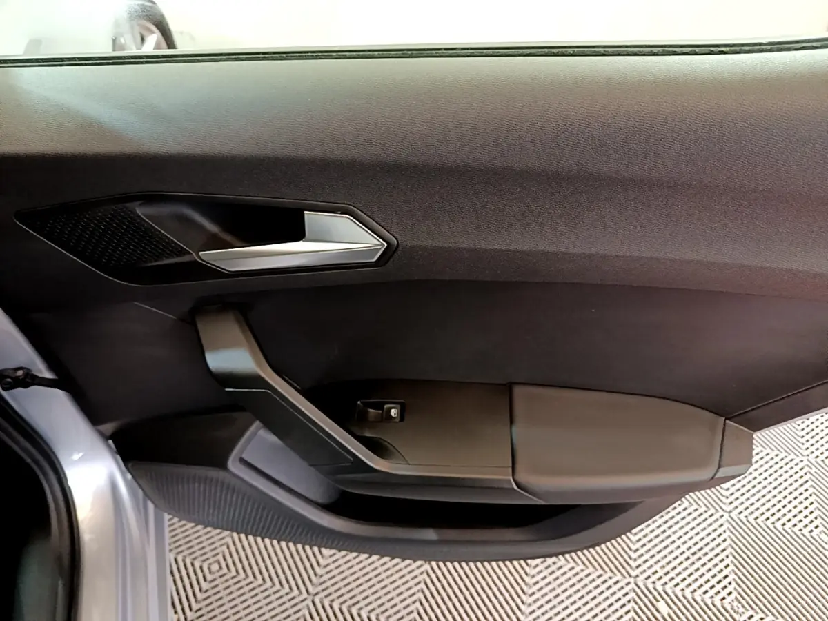 Gros plan sur la porte intérieure côté gauche d'une SEAT Leon gris foncé, avec poignée argentée et commande de vitre.