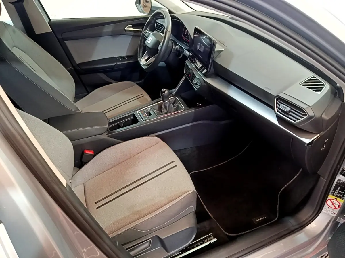 Intérieur avant droit de la SEAT Leon 2023 gris foncé, montrant sièges tissu, volant cuir et écran tactile central.