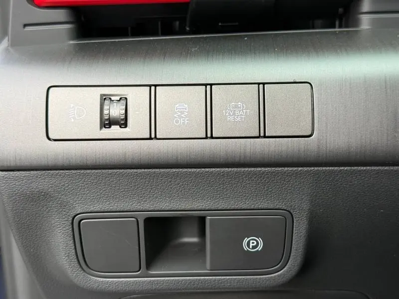 Détail des commandes de tableau de bord gris foncé du Hyundai Kona 2025, avec bouton frein à main électronique.