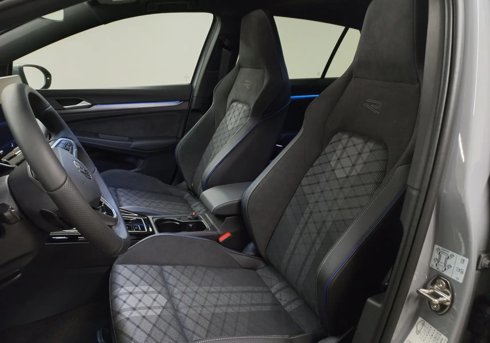 Vue intérieure côté gauche de la Volkswagen Golf 2.0 TDI R-Line 2026 avec sièges sport en tissu gris et surpiqûres bleues.