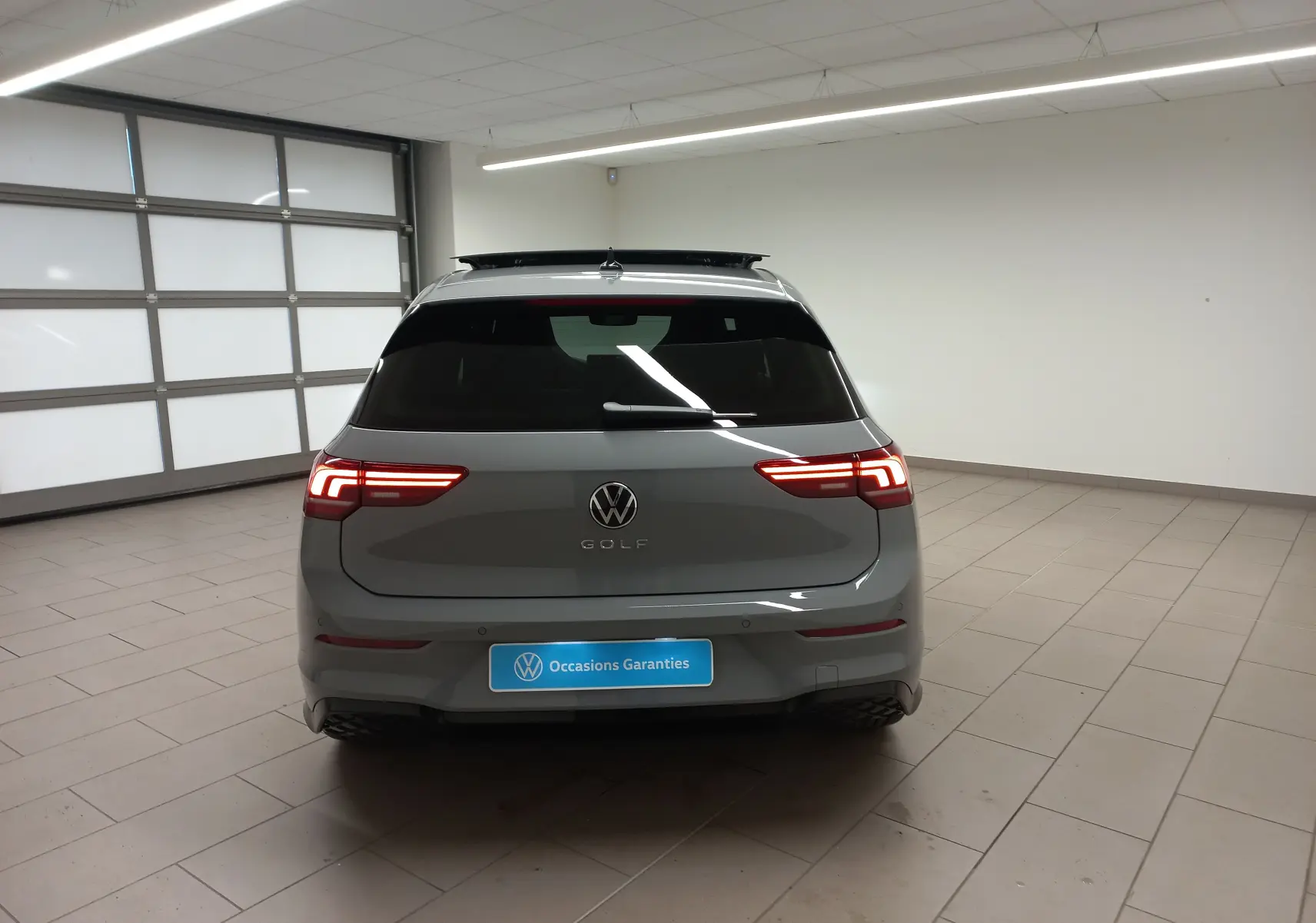 Vue arrière d'une Volkswagen Golf 2.0 TDI R-Line gris lunaire avec toit ouvrant panoramique en intérieur showroom.