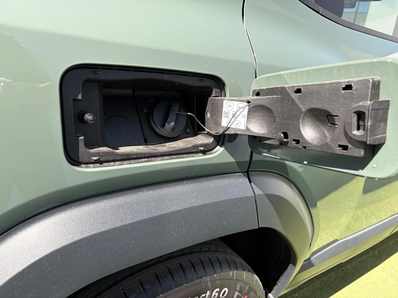 Détail de la trappe à carburant ouverte côté gauche du Dacia Duster III kaki lichen, avec partie arrière du véhicule visible.