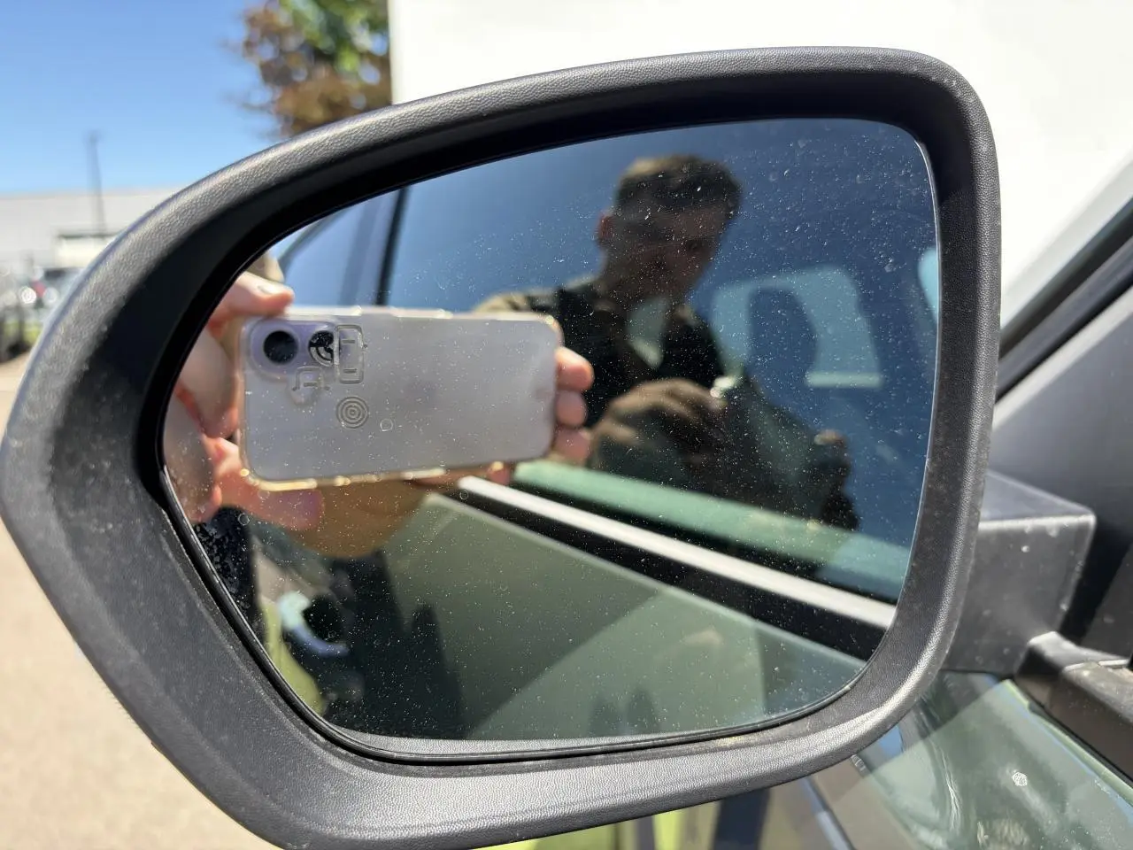 Rétroviseur extérieur côté gauche du Dacia Duster kaki lichen, avec reflet partiel du véhicule et d'une personne.