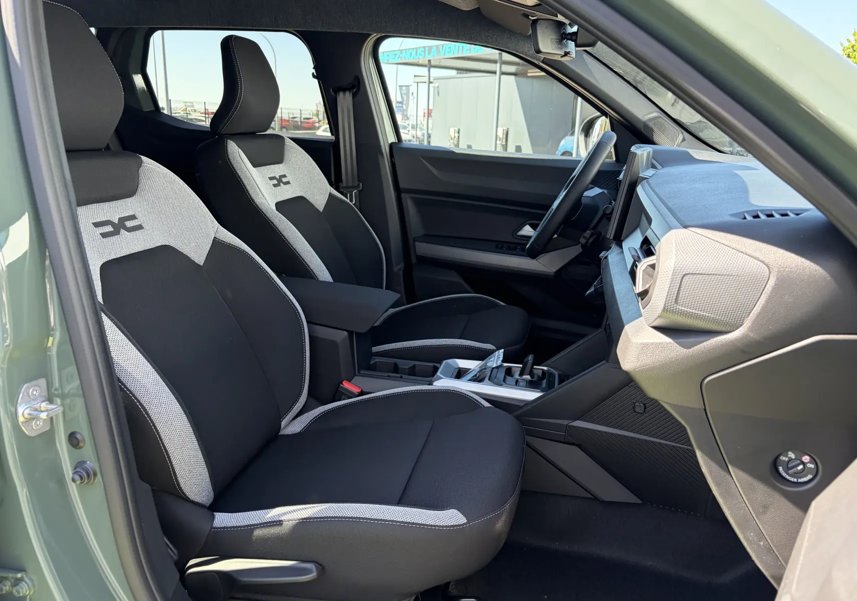 Vue intérieure côté conducteur du Dacia Duster III kaki lichen, mettant en valeur les sièges bi-ton noirs et gris et le tableau de bord moderne.
