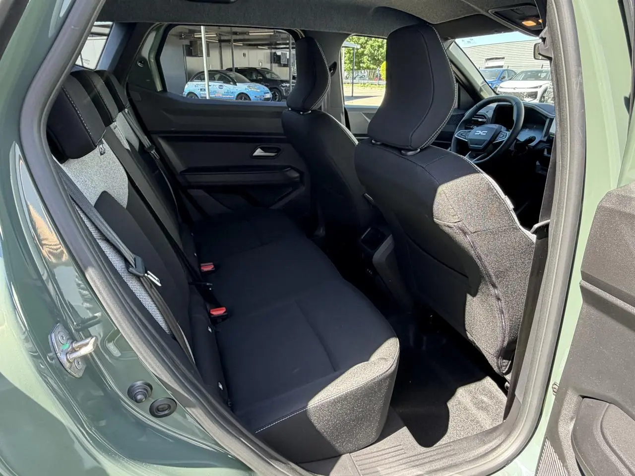 Vue intérieure arrière côté gauche du Dacia Duster III 2026 en kaki lichen, montrant les sièges noirs et l'avant du tableau de bord.
