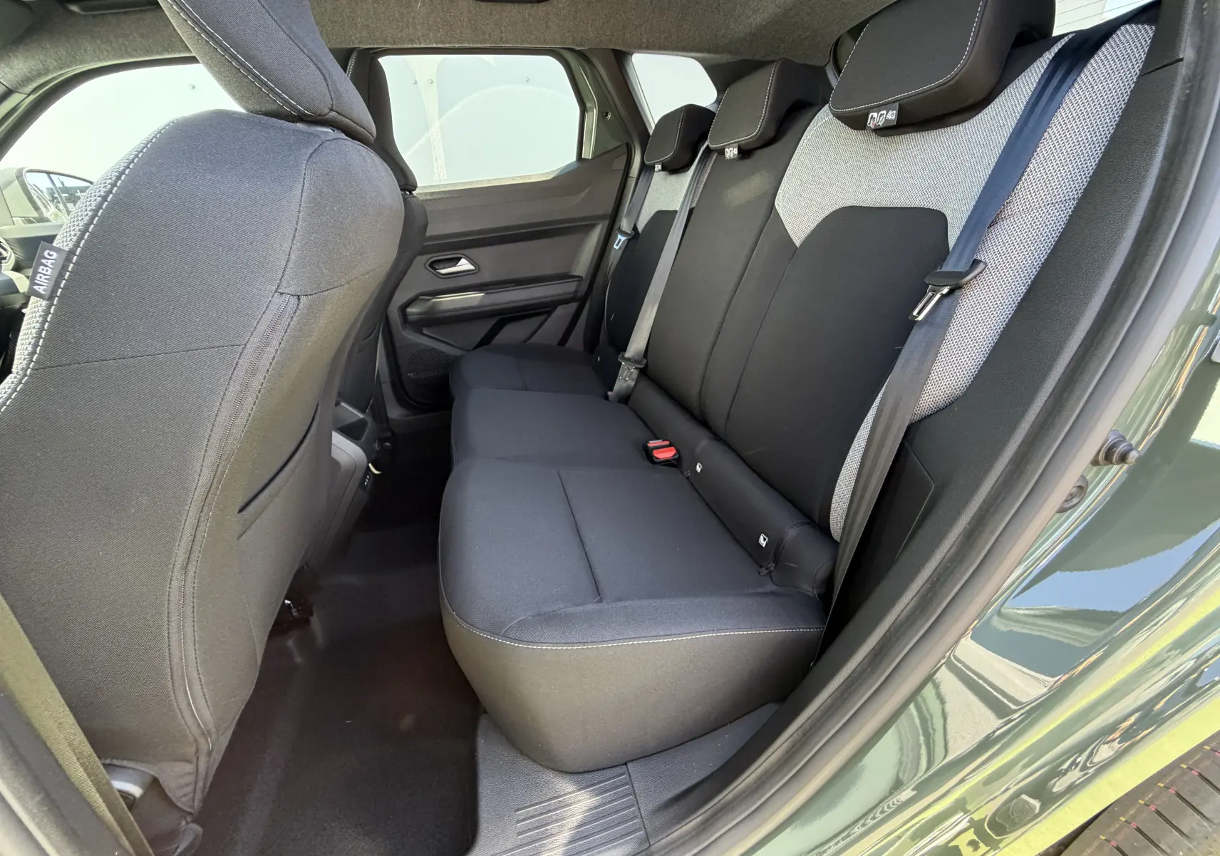 Vue côté droit arrière du Dacia Duster III kaki lichen, montrant la banquette arrière noire avec appuie-têtes intégrés et ceinture de sécurité.