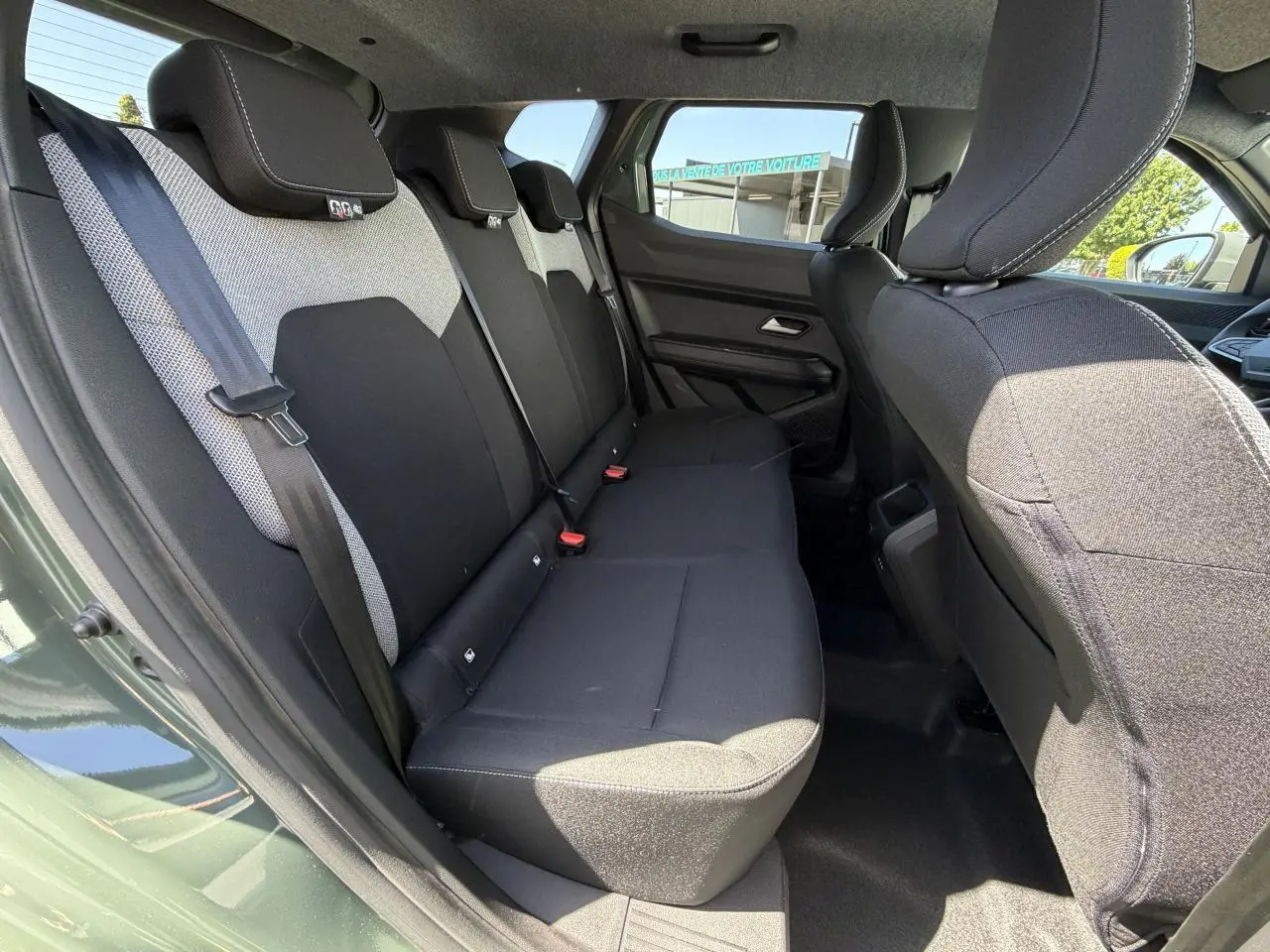 Vue latérale gauche de l'habitacle arrière du Dacia Duster III hybride en kaki lichen, montrant les sièges tissu bicolores.