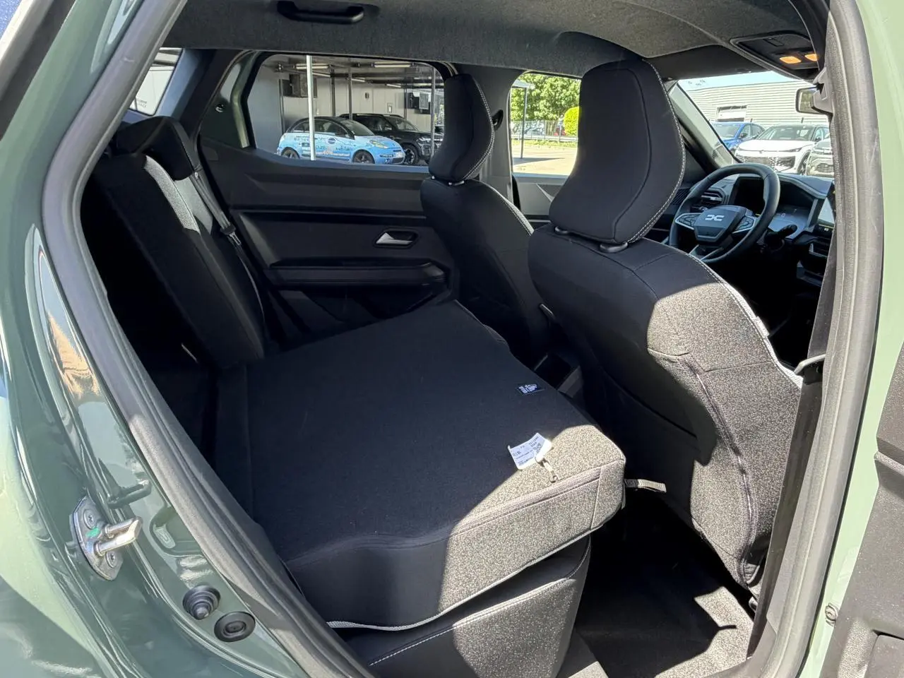 Vue intérieure arrière gauche du Dacia Duster III kaki lichen, banquette rabattue et sièges avant noirs visibles.