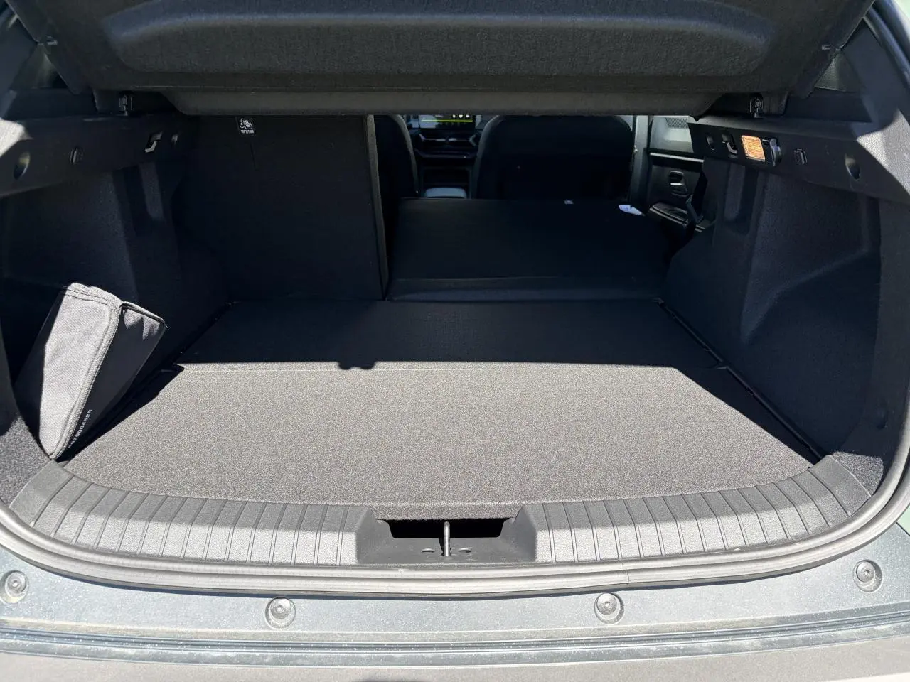 Vue du coffre ouvert du Dacia Duster III 1.8 Hybrid 155, montrant la banquette arrière rabattue et le tapis de coffre gris.