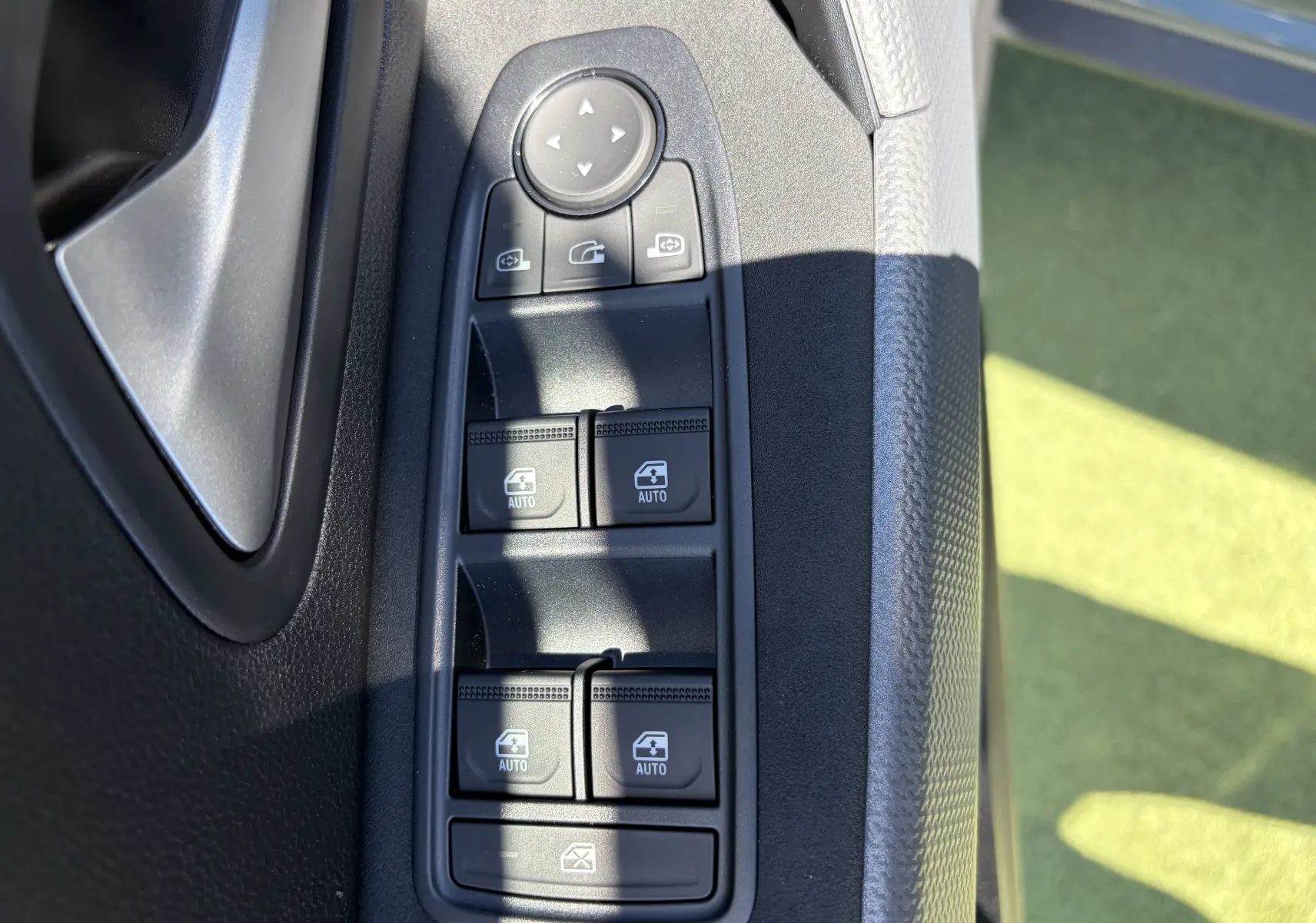 Gros plan sur les commandes des vitres électriques et des rétroviseurs côté conducteur du Dacia Duster kaki lichen.