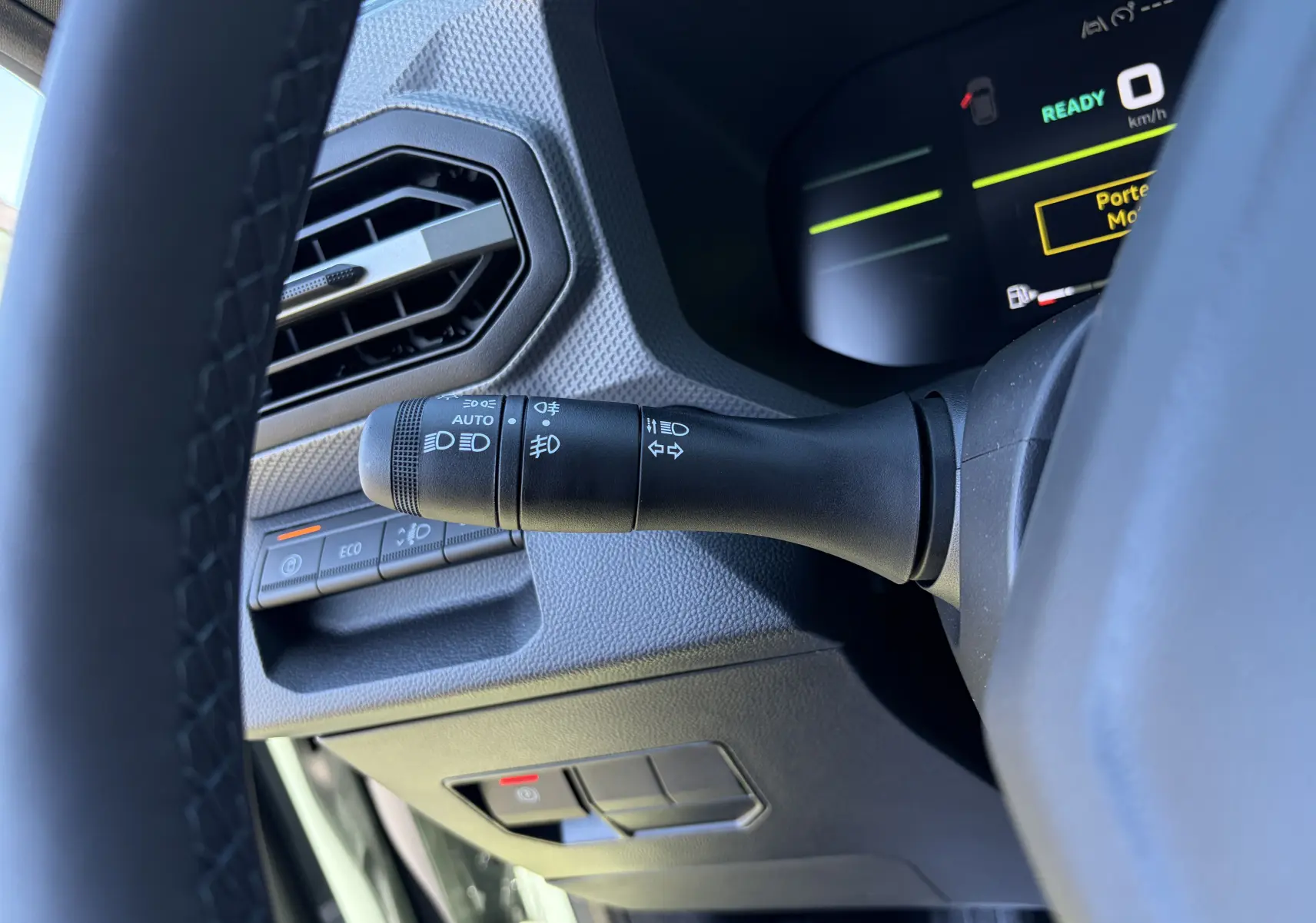 Gros plan côté gauche du volant du Dacia Duster III kaki, montrant la commande des phares et l'aération hexagonale.