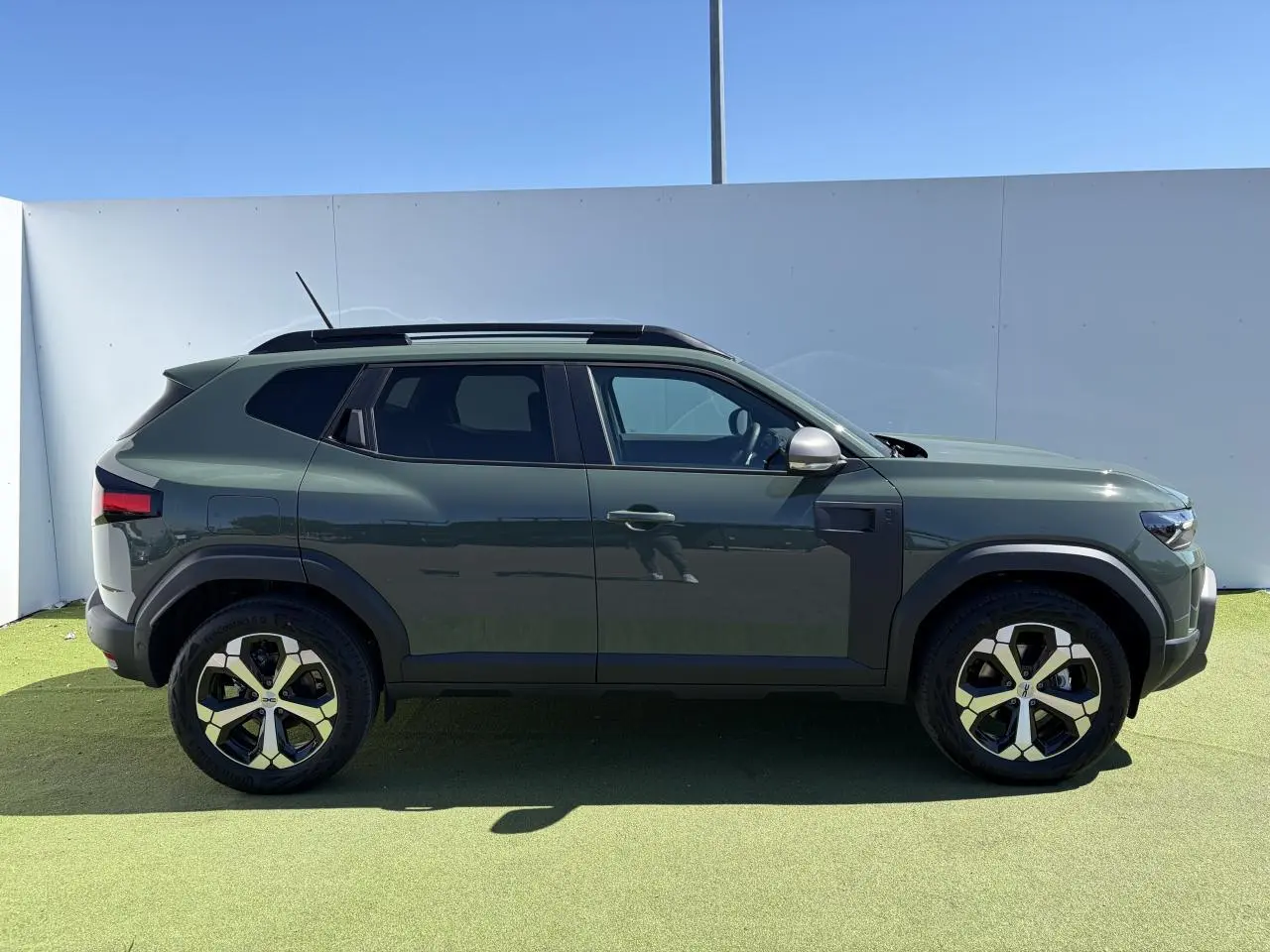 Vue de profil côté gauche d'un Dacia Duster III 2026 en kaki lichen avec jantes alliage 18 pouces diamantées.