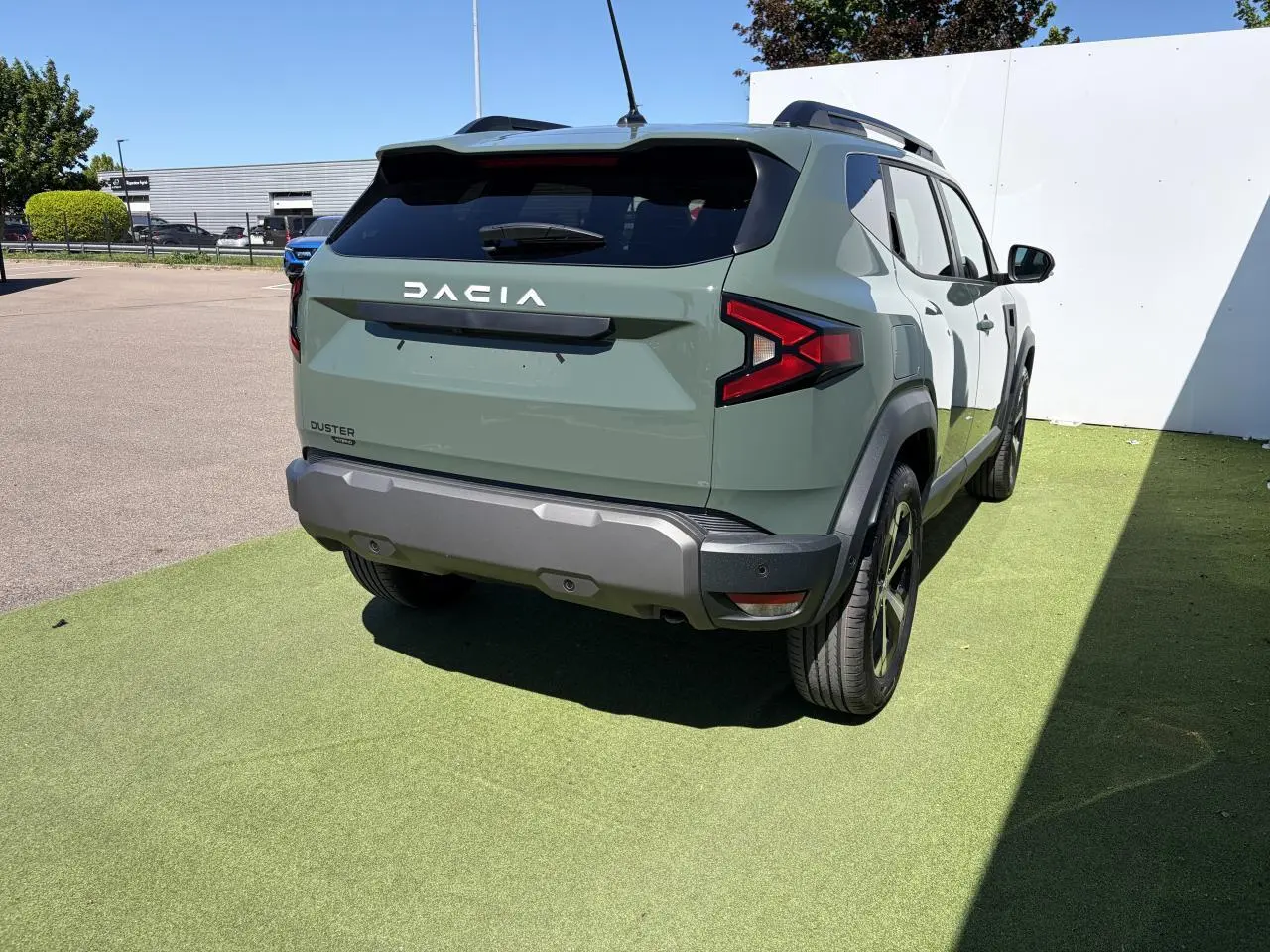 Vue 3/4 arrière droite du Dacia Duster III hybride en kaki lichen, avec barres de toit noires et jantes alliage 18 pouces.