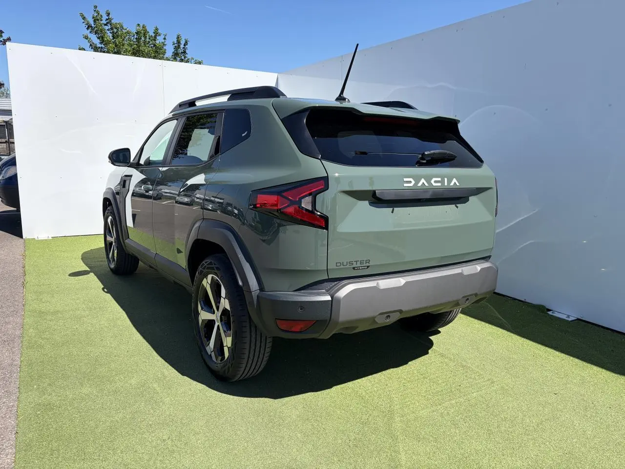 Vue 3/4 arrière droite du Dacia Duster III hybride en kaki lichen avec jantes alliage et barres de toit noires.