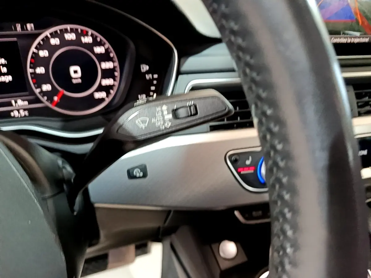 Gros plan sur le volant cuir et le tableau de bord numérique de l'Audi A4 noire, avec commandes de climatisation visibles.