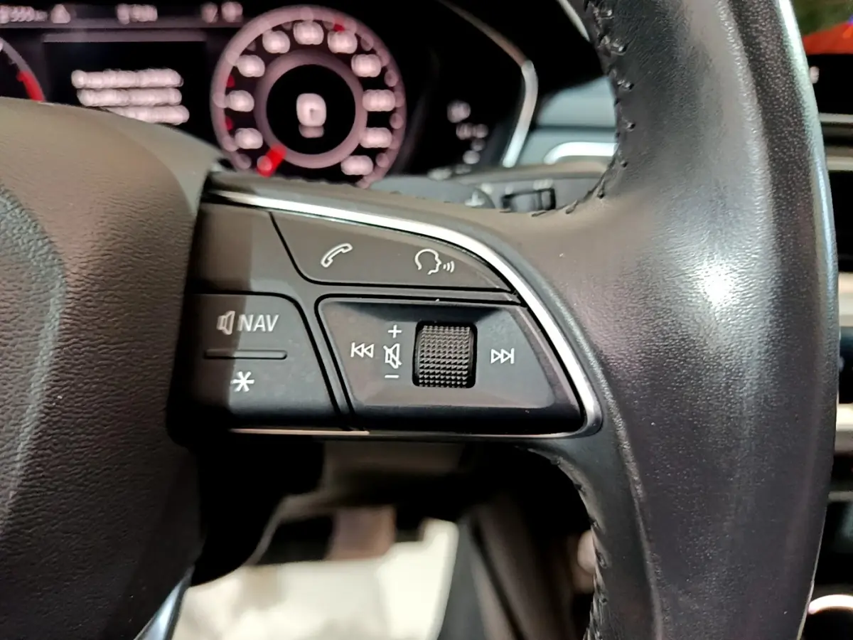 Gros plan sur les commandes gauche du volant cuir noir de l'Audi A4 40 TDI 2018 avec tableau de bord numérique en arrière-plan.