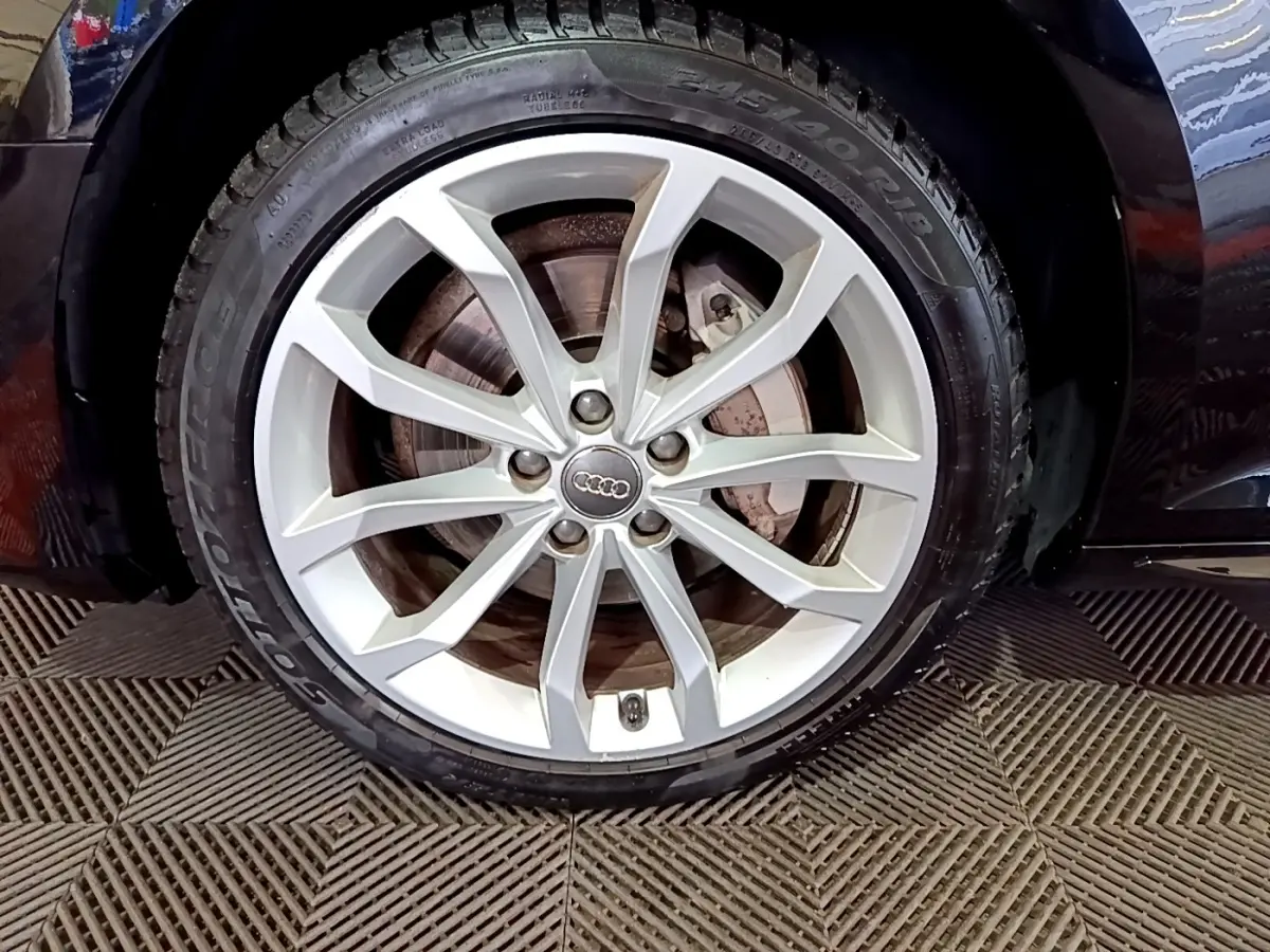 Gros plan sur la roue avant droite avec jante argentée de l'Audi A4 noire 40 TDI 2018 Design Luxe.