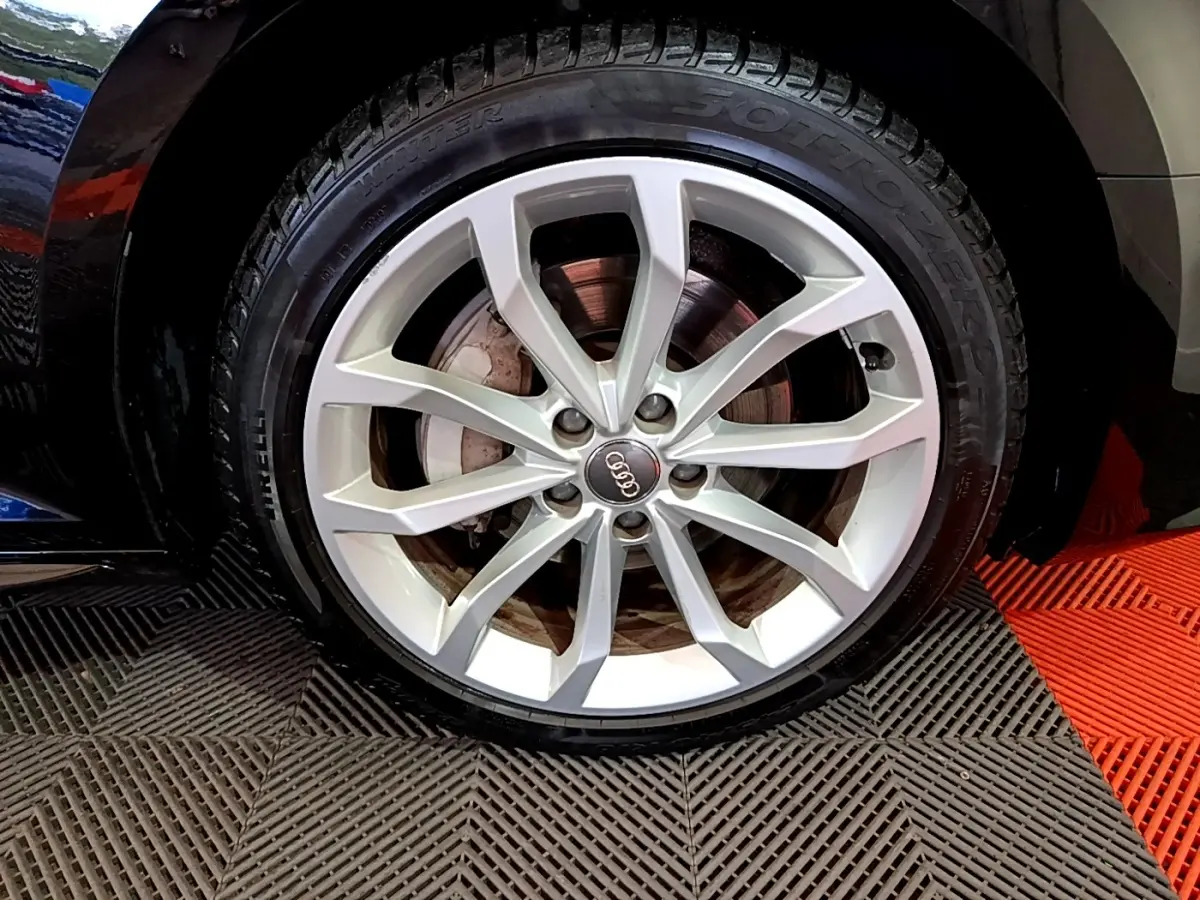 Gros plan sur la jante argentée et pneu Pirelli d'une Audi A4 noire, mettant en valeur le logo Audi central.