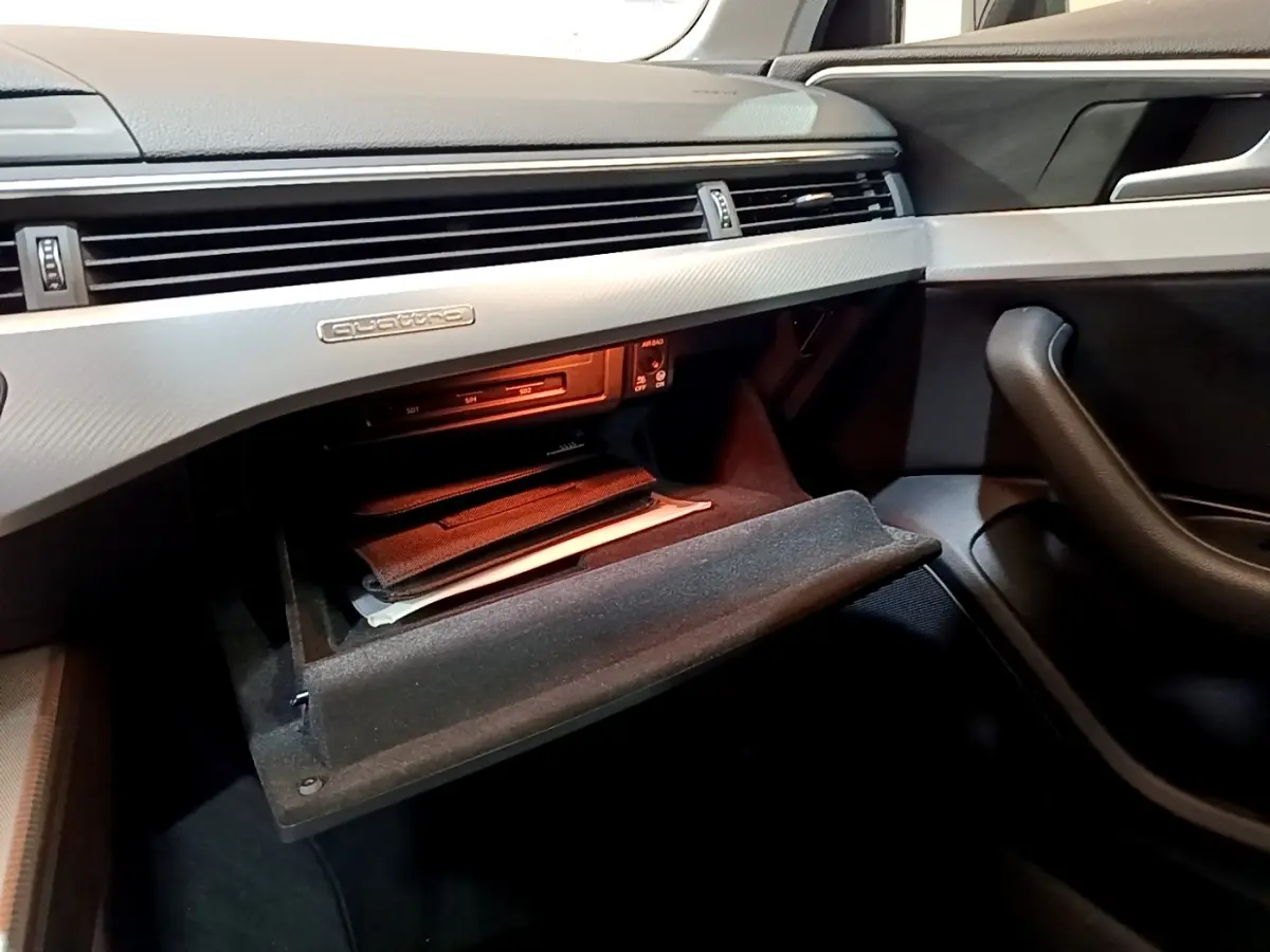 Intérieur côté passager de l'Audi A4 noire 2018, boîte à gants ouverte avec badge Quattro sur tableau de bord gris.