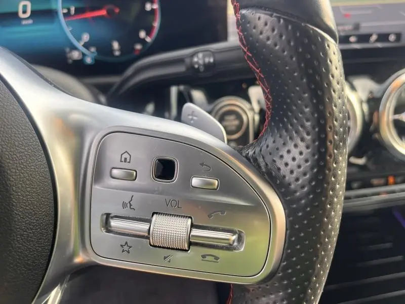 Gros plan sur la partie gauche du volant cuir perforé avec commandes volume et fonctions multimédia du Mercedes GLA gris montagne magno.