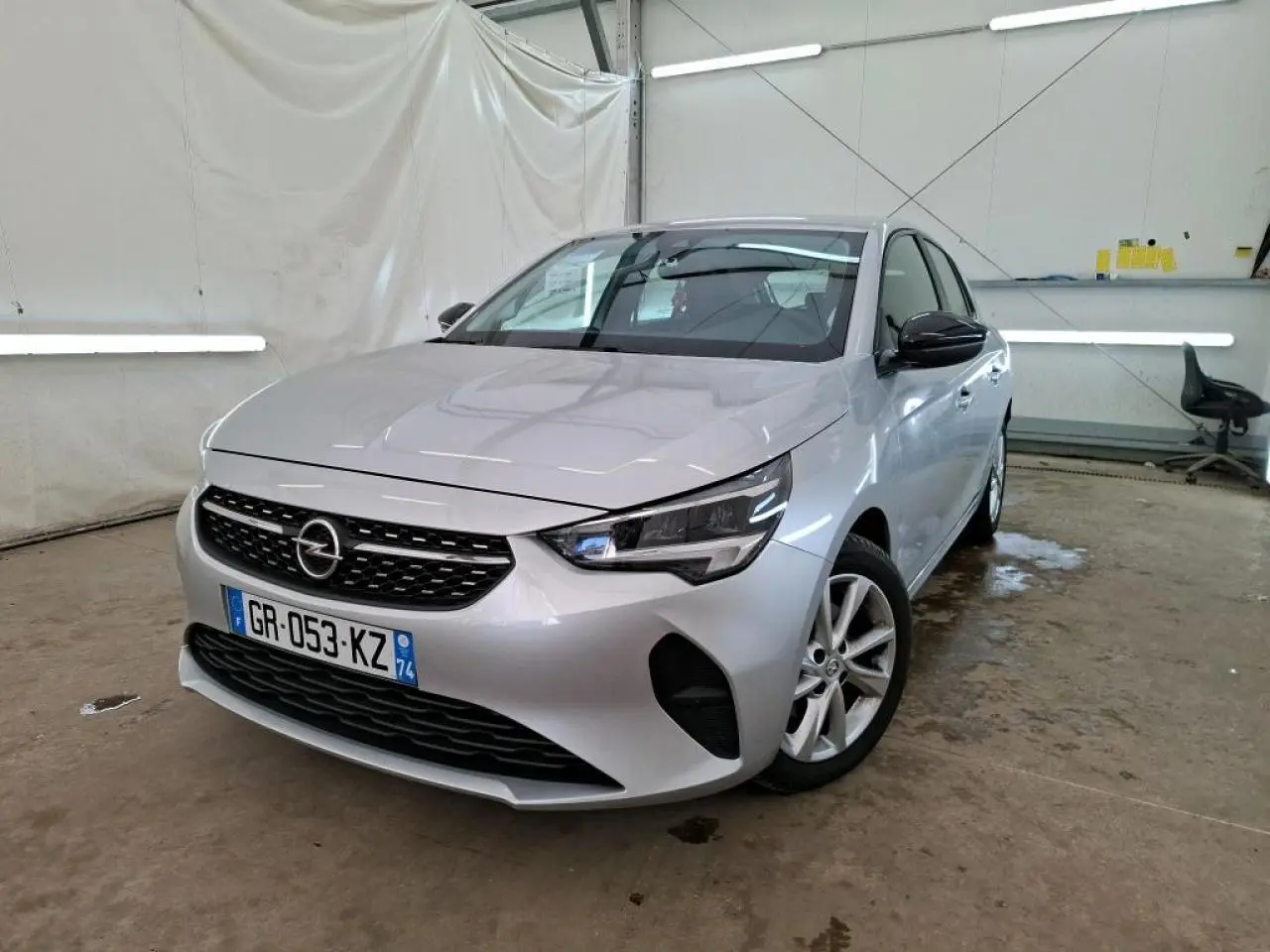 Opel Corsa gris clair vue 3/4 avant droit, avec jantes alliage 16'' et rétroviseurs noirs dans un garage.
