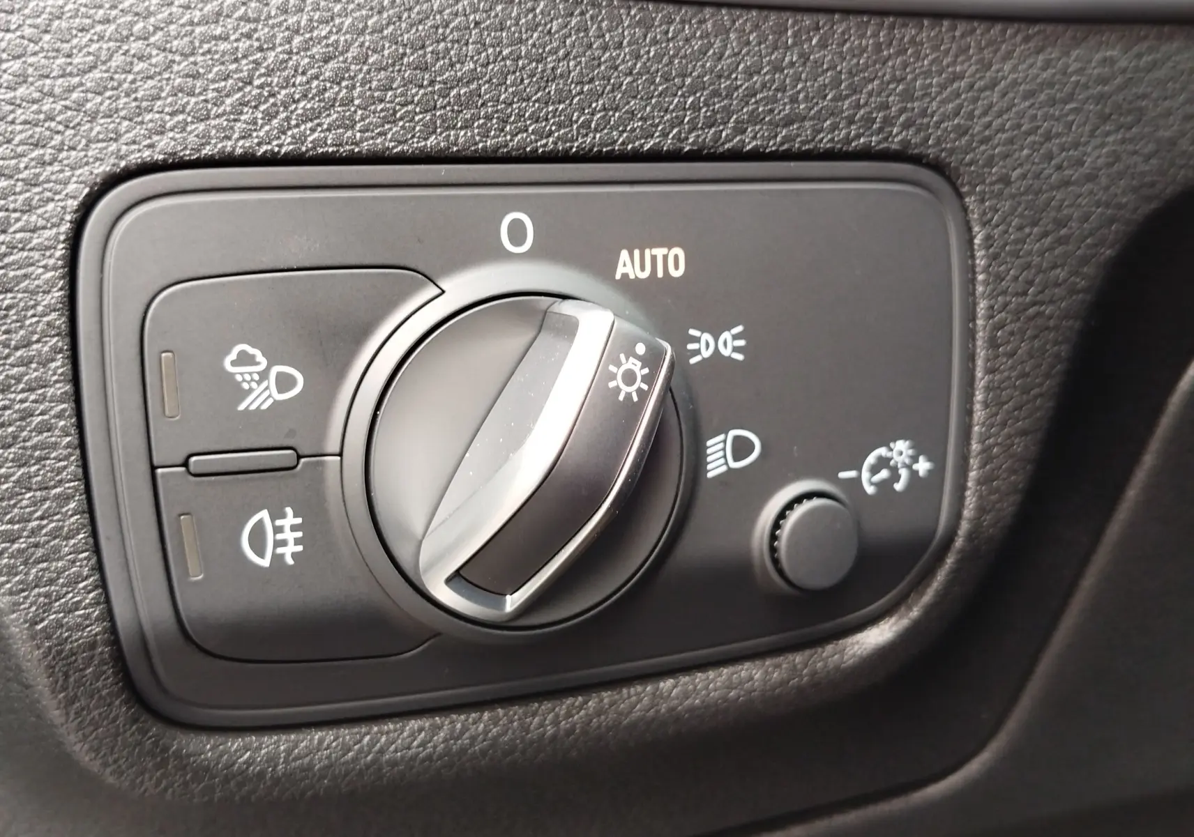 Gros plan sur le sélecteur de feux avec réglage automatique dans l’habitacle noir de l’Audi Q2 35 TFSI S line 2023.