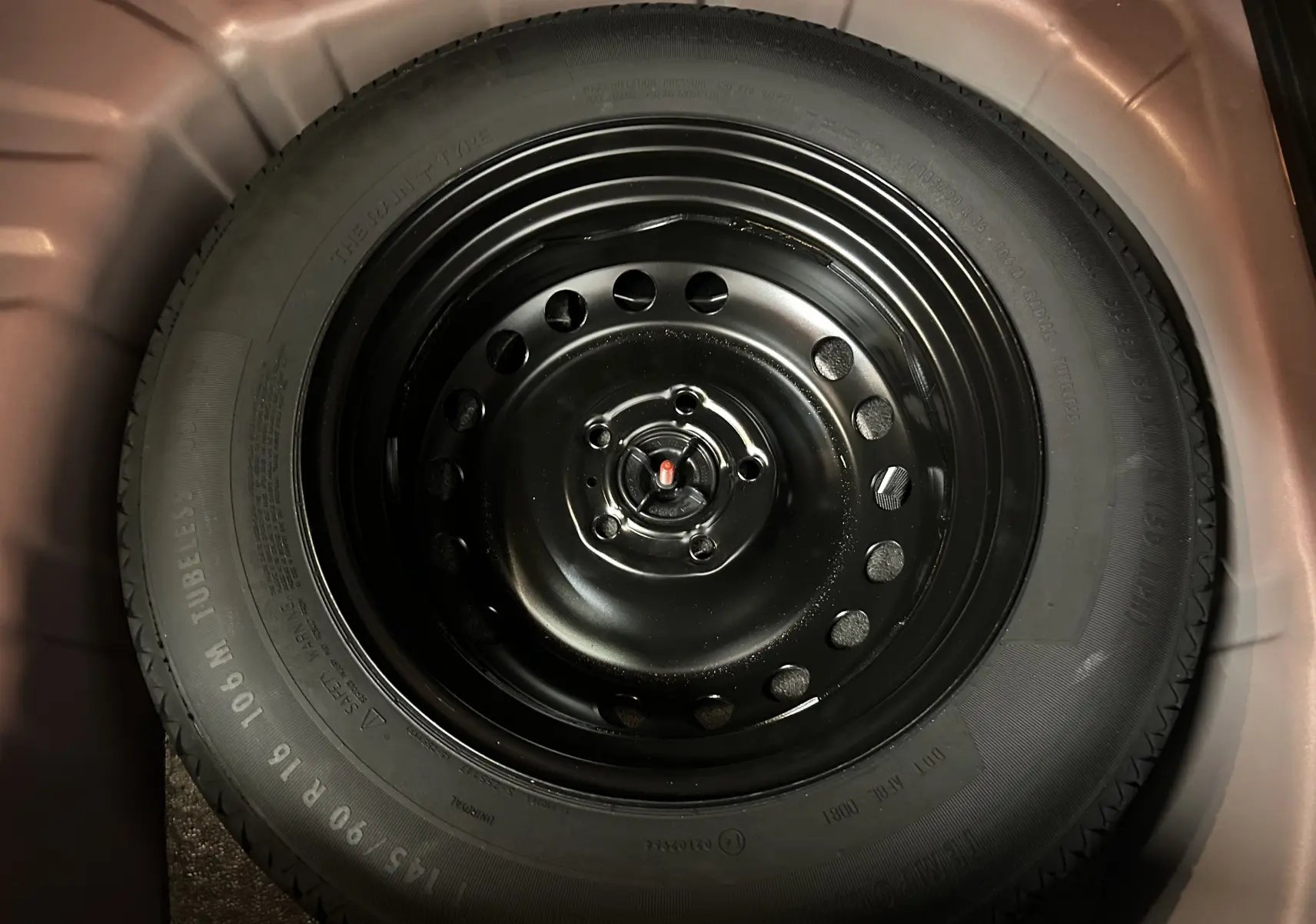 Roue de secours noire en acier du Renault Captur TCE 90CH TECHNO 2024, vue en gros plan dans le coffre.