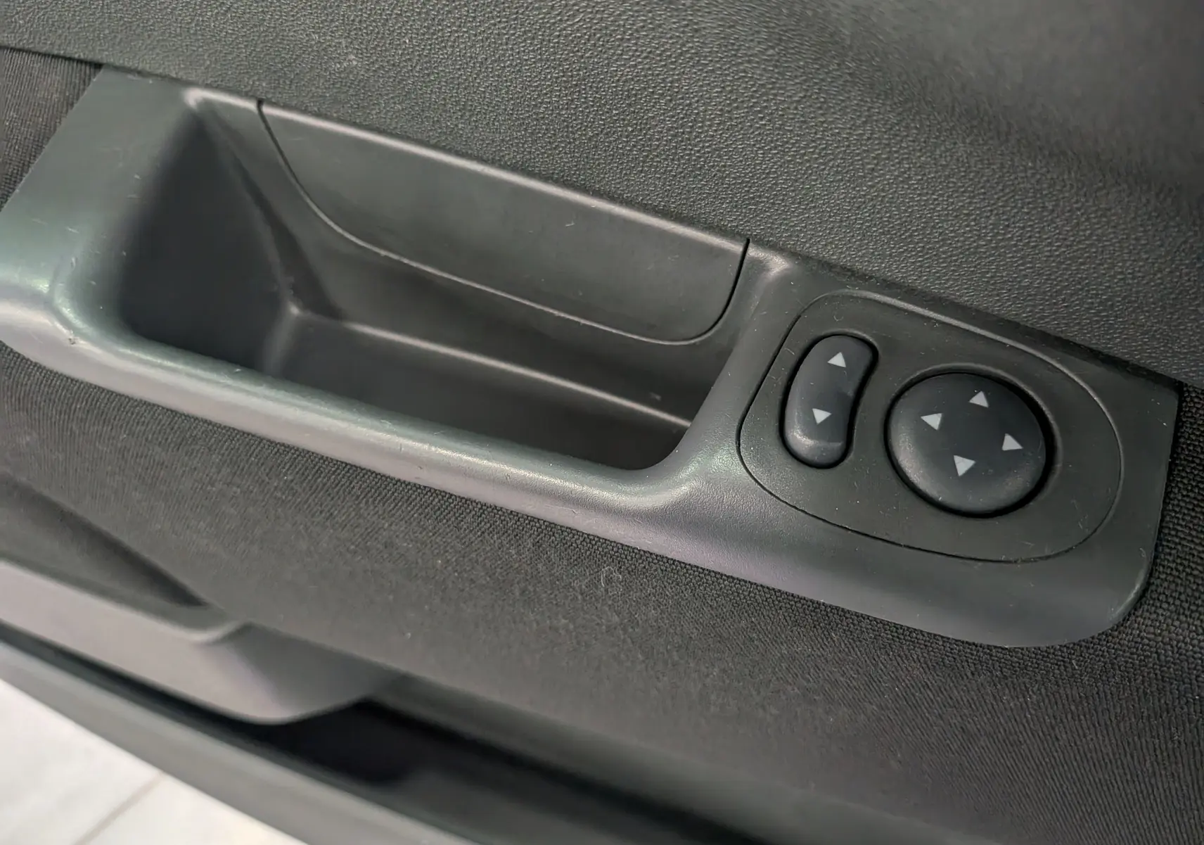 Gros plan sur la commande de réglage des rétroviseurs côté gauche de la porte intérieure noire d'une Fiat 500.