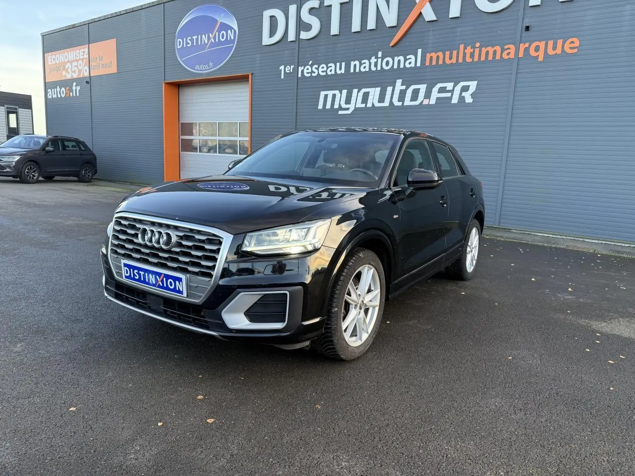 Audi Q2 noir brillant vue 3/4 avant droit avec calandre chromée et jantes argentées sur parking extérieur.