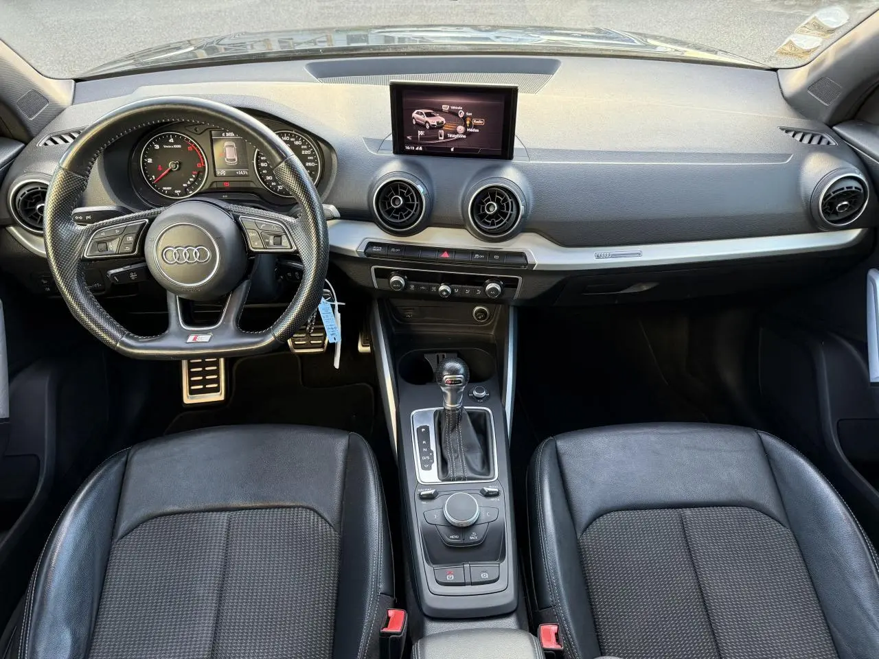 Vue intérieure avant de l'Audi Q2 S Line 2019 avec volant cuir multifonction noir et console centrale avec boîte auto.