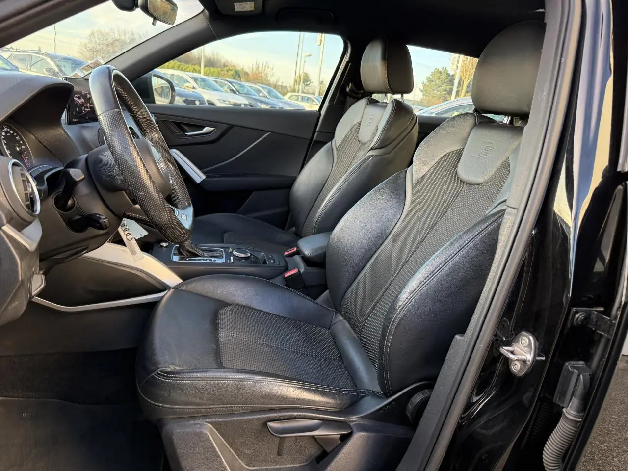 Intérieur noir de l'Audi Q2 S line 2019 vu côté conducteur, avec sièges sport en cuir et volant multifonction.