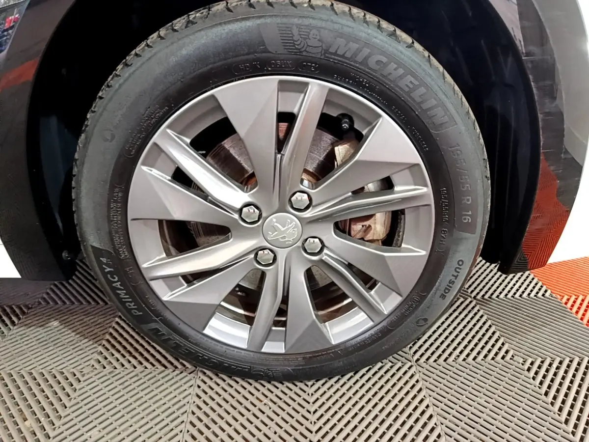 Gros plan sur la roue avant droite d'une Peugeot 208 électrique blanche, jante alliage avec logo lion central.