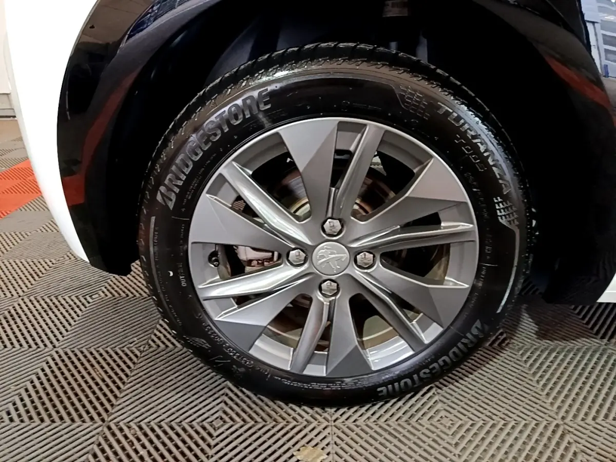 Gros plan sur la roue avant droite d'une Peugeot 208 électrique blanche, jante alliage gris argenté et pneu Bridgestone.