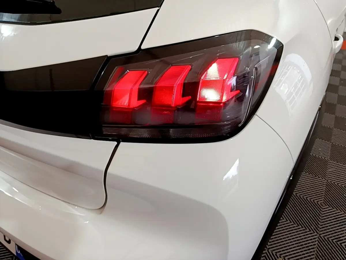Gros plan sur le feu arrière droit rouge d'une Peugeot 208 électrique blanche, avec carrosserie brillante et détails noirs.