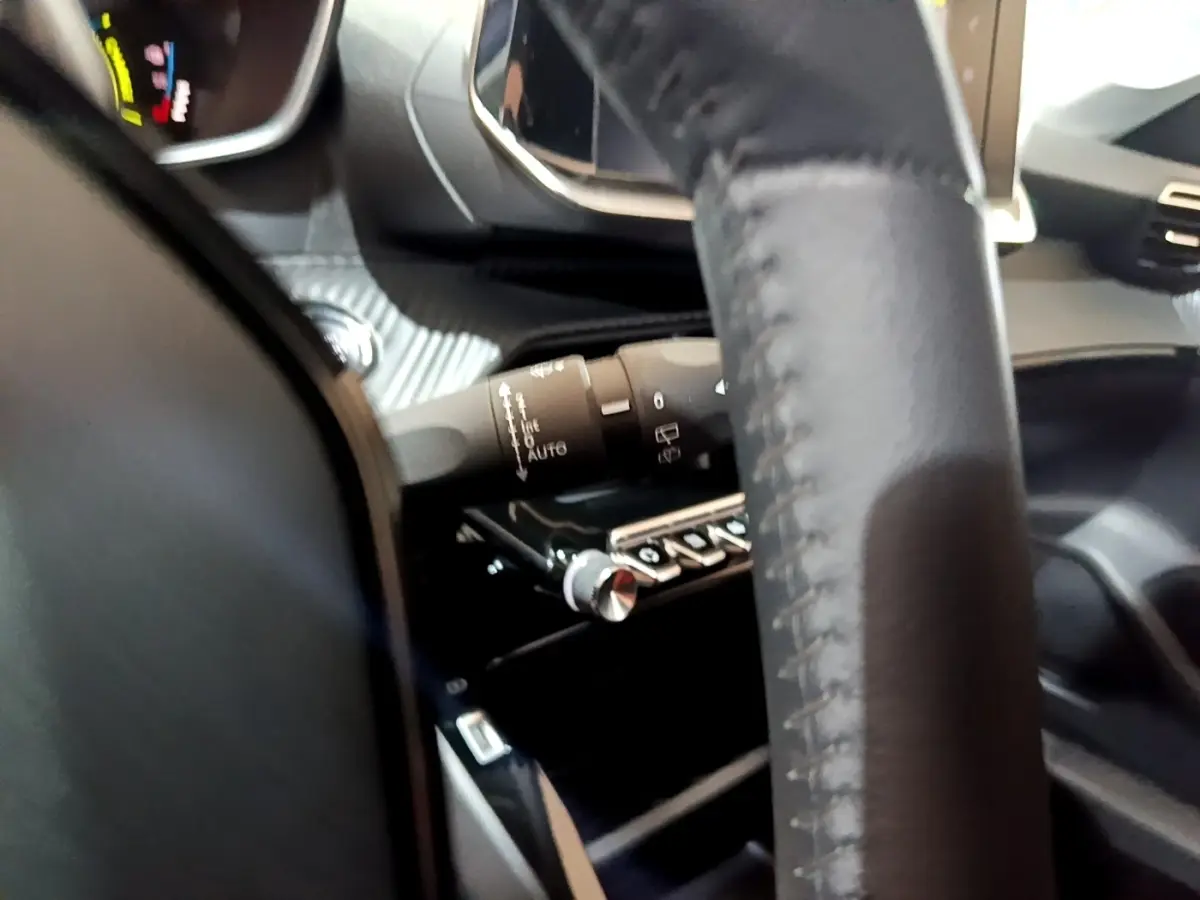 Gros plan sur le volant cuir et la commande des essuie-glaces du tableau de bord d'une Peugeot 208 électrique blanche.