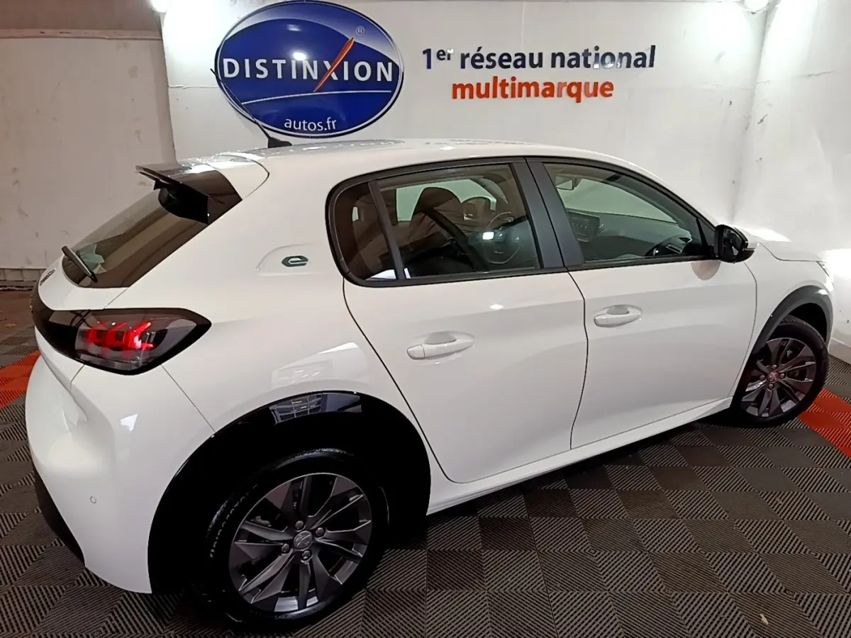 Vue 3/4 arrière droite d'une Peugeot 208 électrique Active Business blanche avec jantes foncées et logo "e" vert sur l'aile arrière.