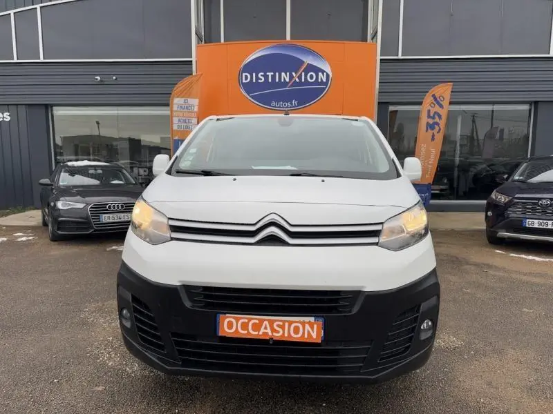 Vue avant d'un Citroën Jumpy blanc Banquise avec calandre noire et plaque orange "OCCASION" devant un concessionnaire.