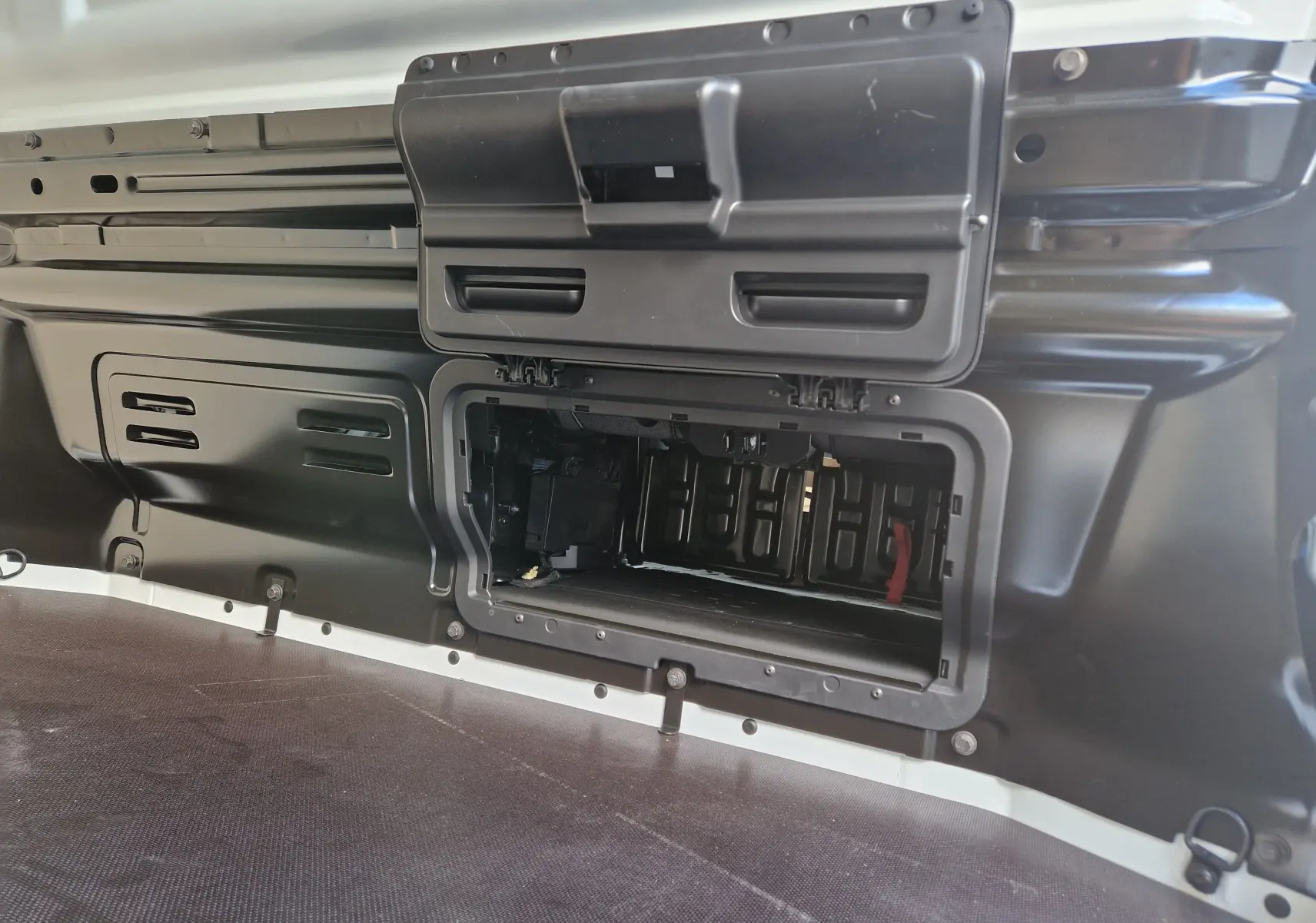 Détail du compartiment de rangement ouvert dans la zone de chargement noire du Nissan Primastar blanc 2025.